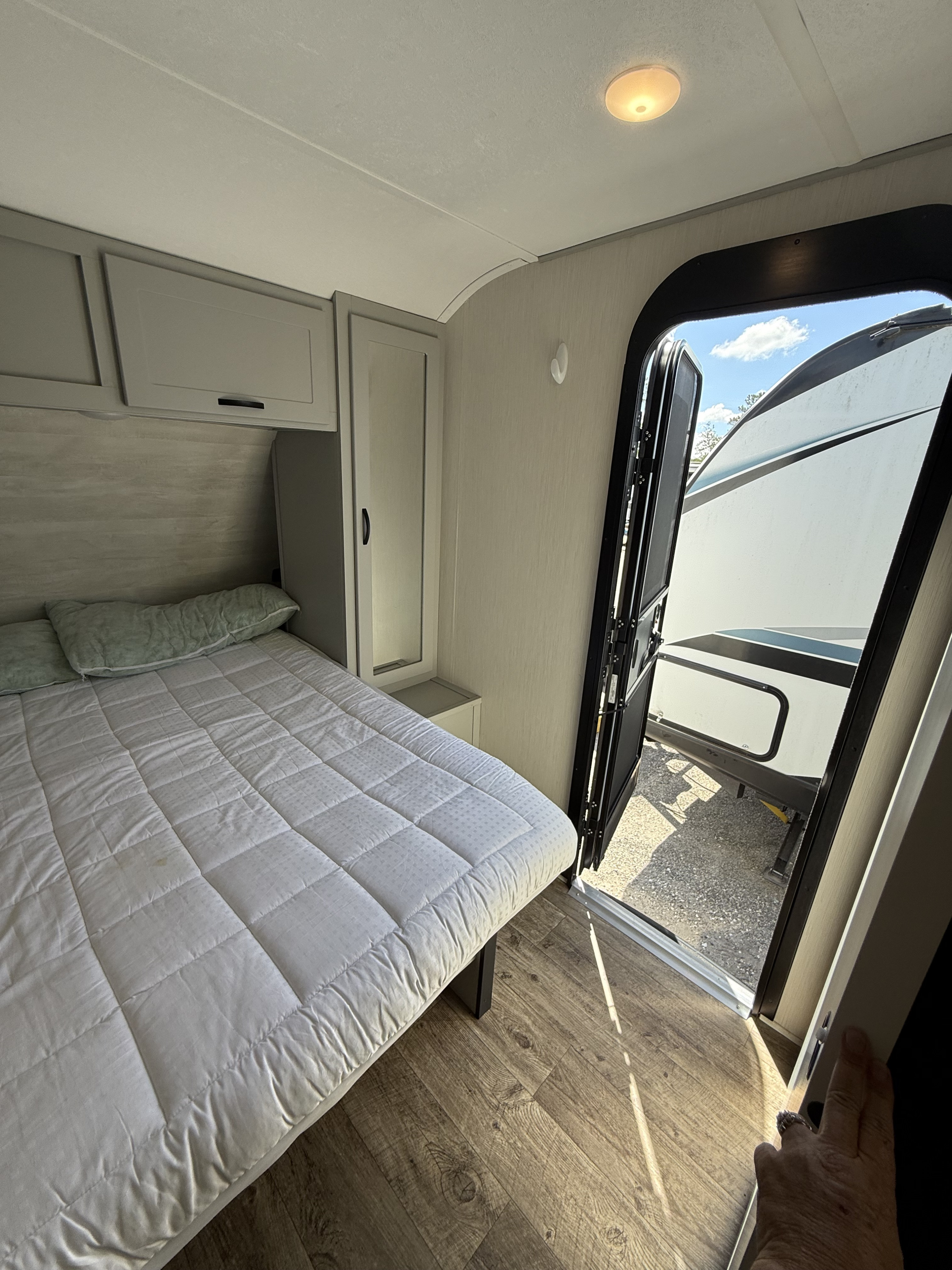 Cozy RV rental bedroom with a comfy bed, gray cabinets, and an open door showing the outside view.. Forest River Vibe 2023