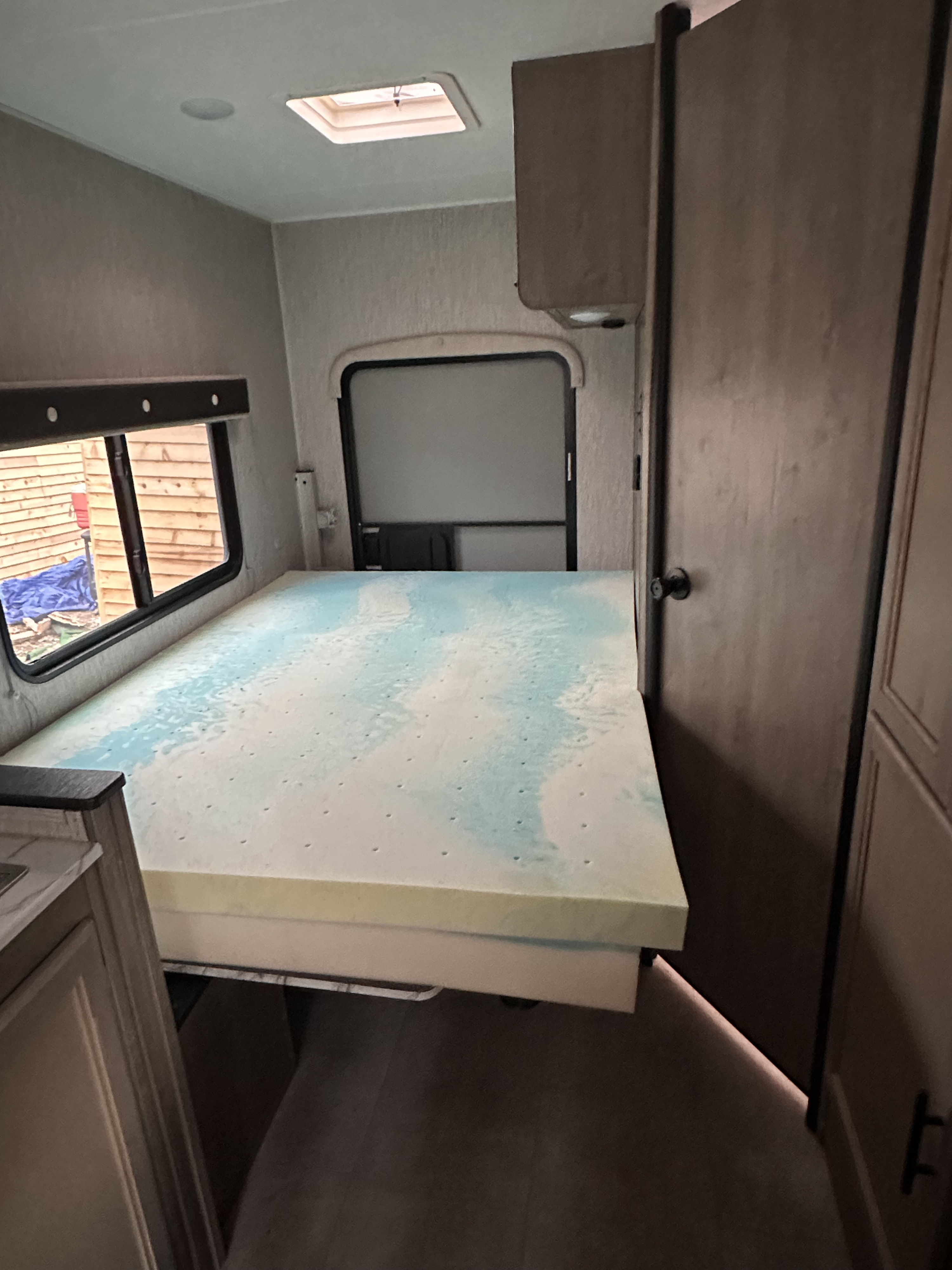 Inside this RV rental, a compact bedroom features a bed with a blue memory foam topper, windows, and an interior door.. Coachmen Cross Trek 2021
