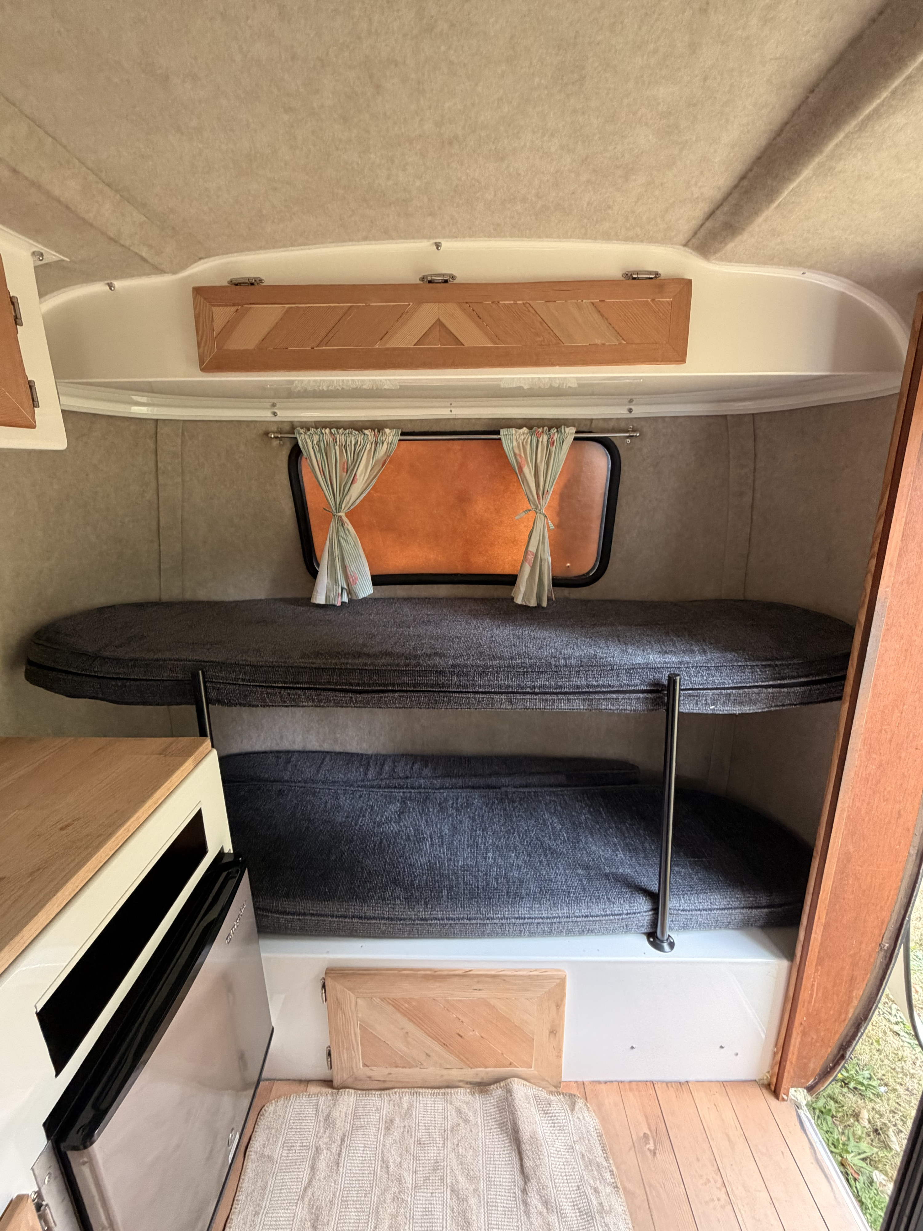 This rv rental shows a cozy bunk bed sleeping area, small kitchen counter, and window with curtains in a compact interior.. Scamp Scamp Trailer 2012