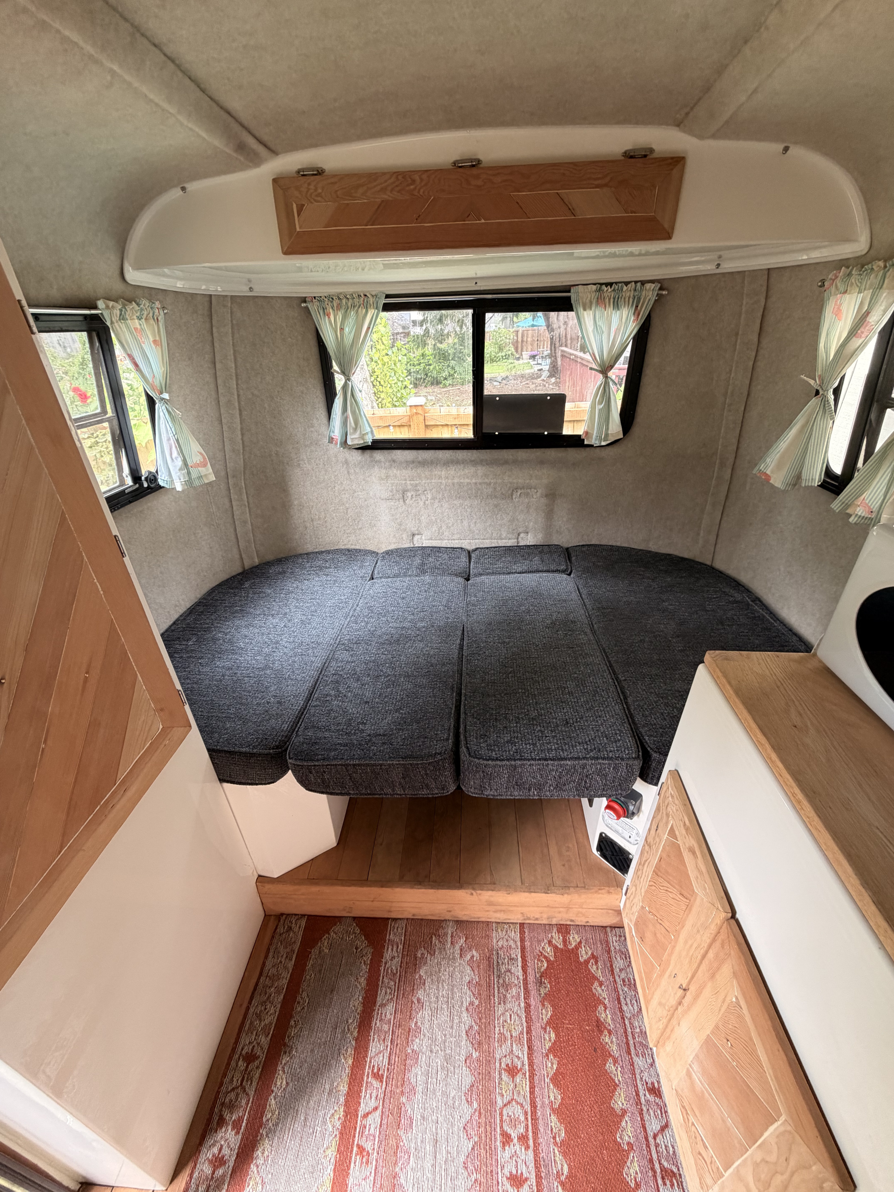 Cozy rv rental interior with a versatile bed/seating area, bright windows, wood accents, and a floor rug.. Scamp Scamp Trailer 2012