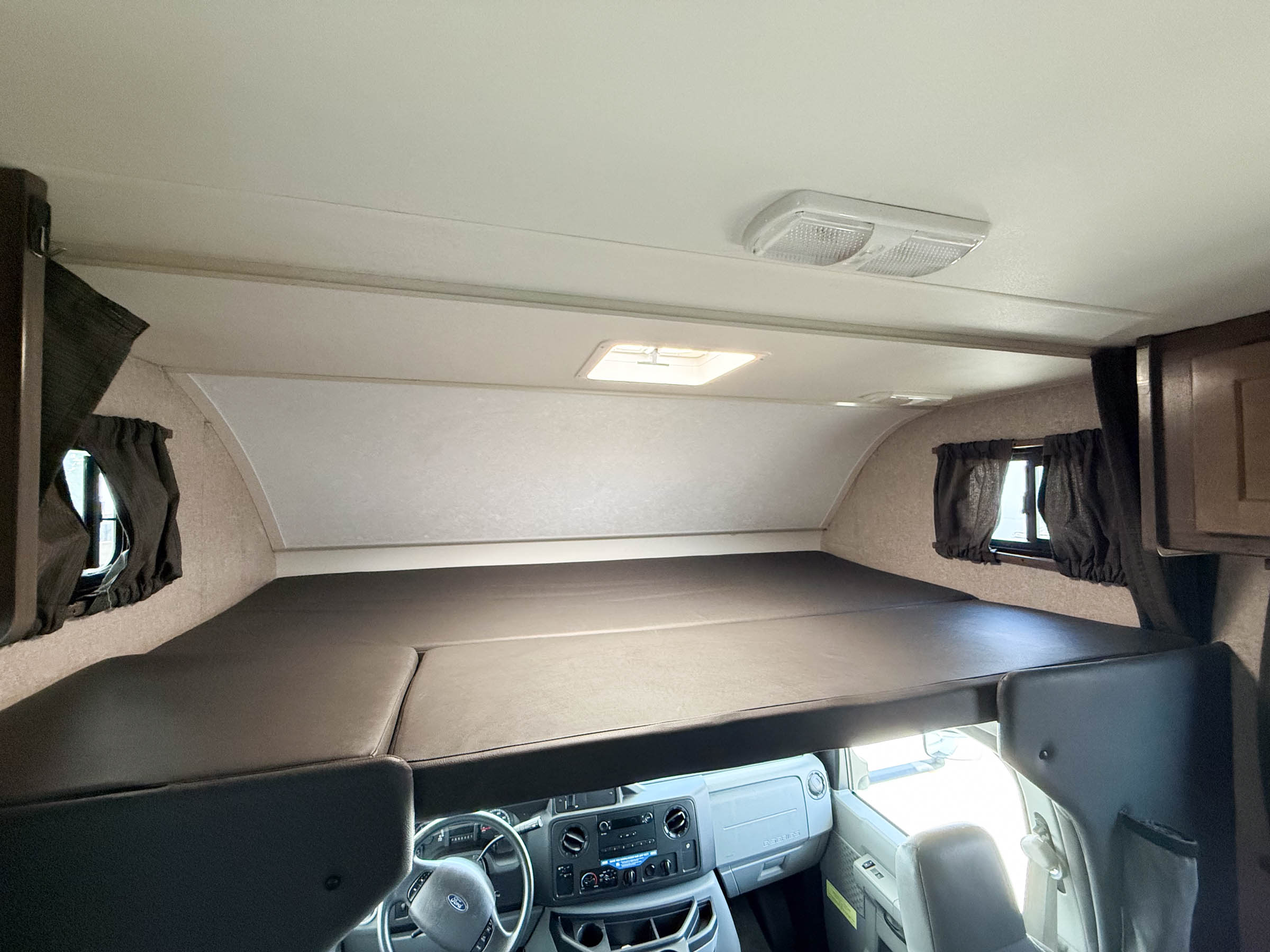 Interior of an rv rental showing the spacious cab-over sleeping bunk and front dashboard. Well-lit and ready for trips.. Winnebago 325AR 2020