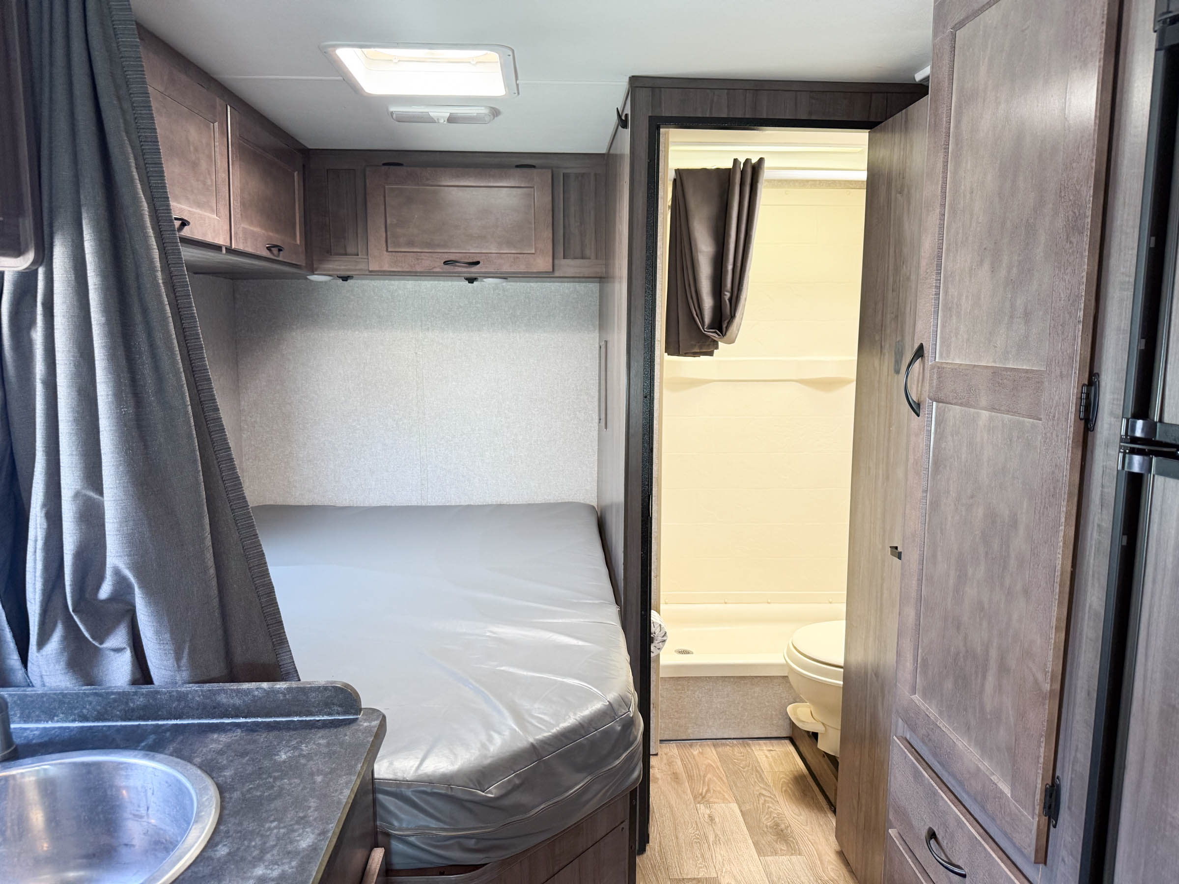 Cozy rv rental interior: a bedroom with a bed, overhead cabinets, sink area, and a view into the compact bathroom.. Winnebago 325AR 2020