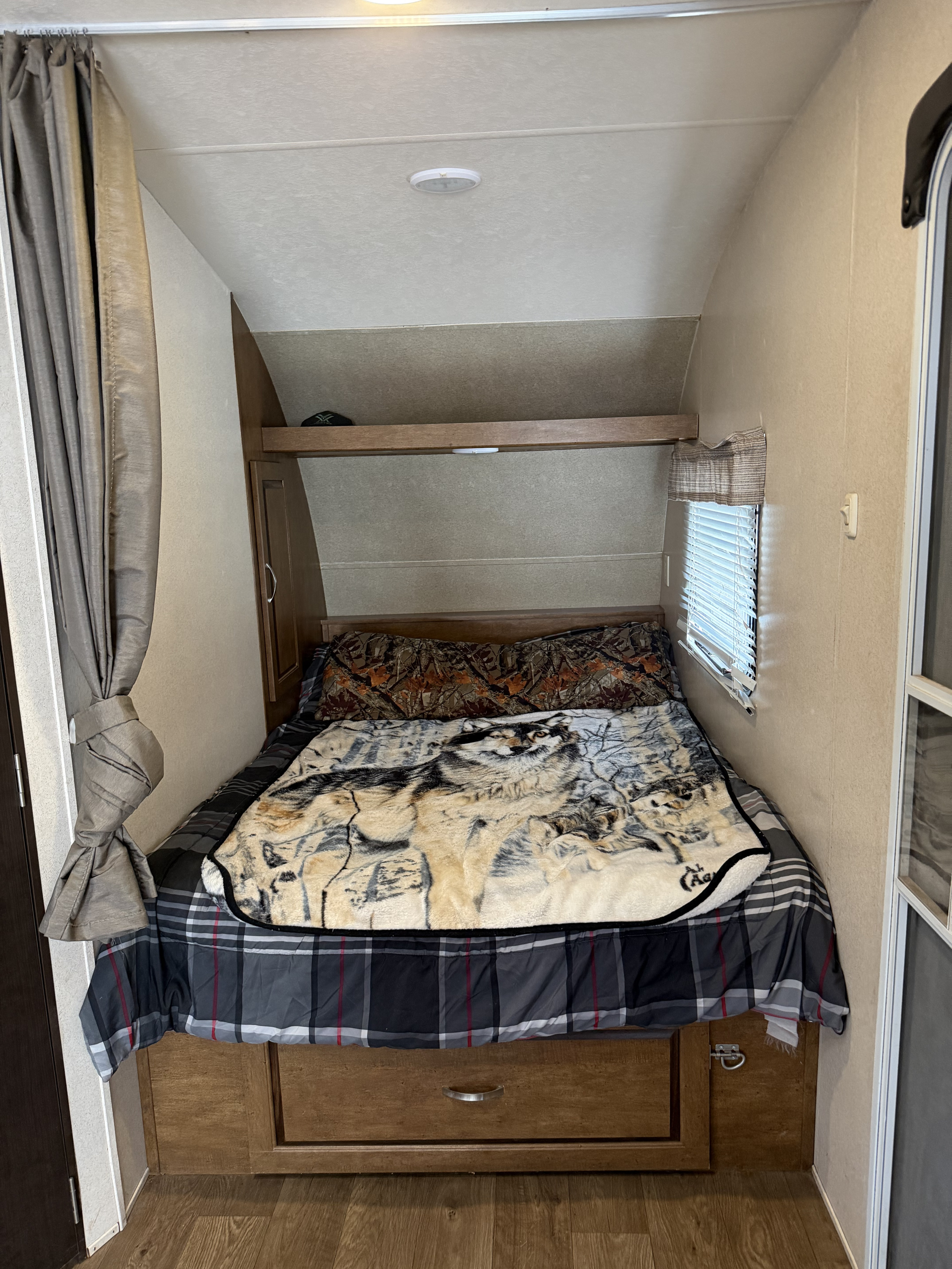 Cozy RV rental bedroom featuring a bed with a wolf blanket, camouflage pillow, and built-in storage. Ideal for travel adventures.. Forest River Salem Cruise Lite 2018