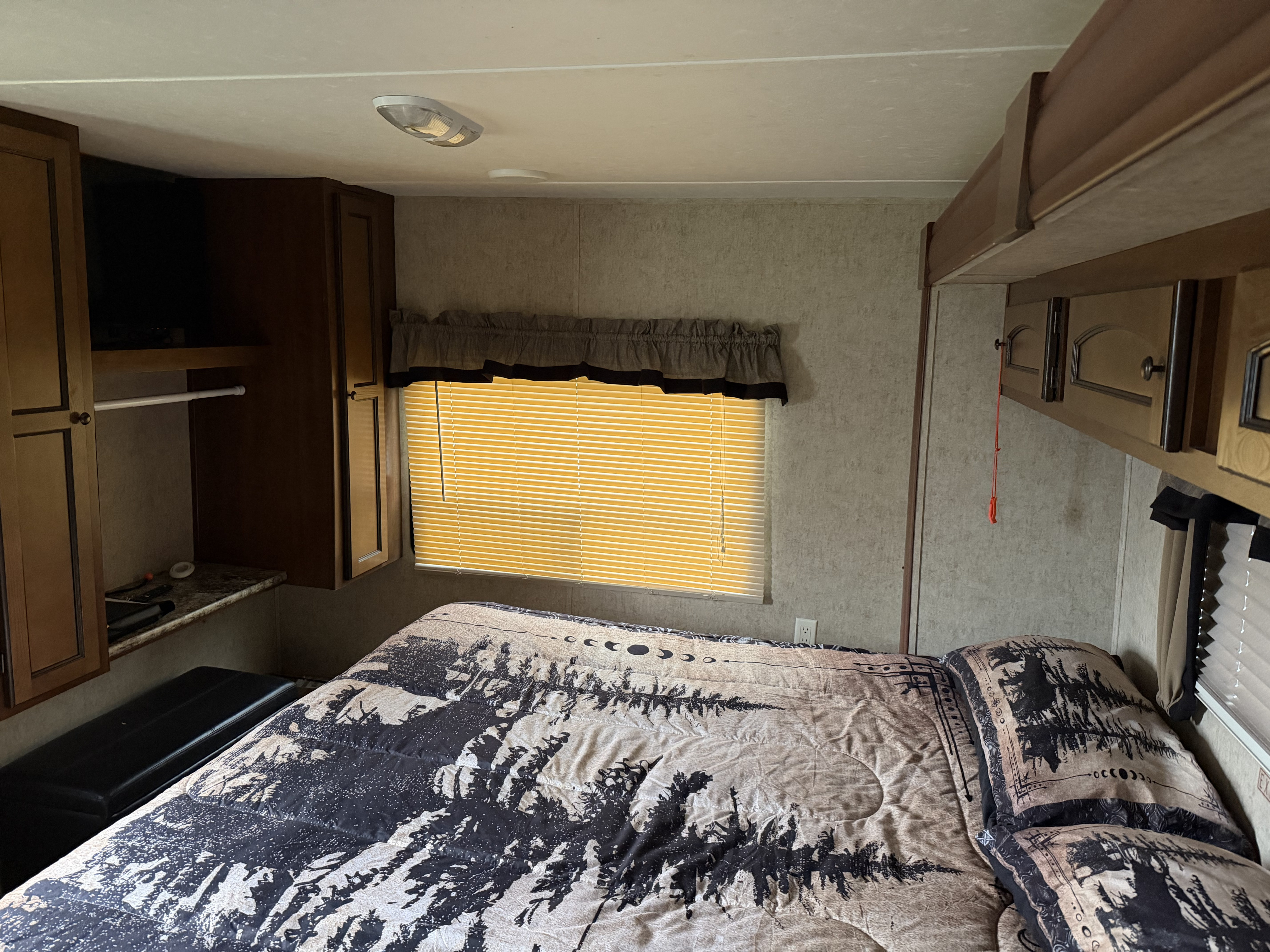 Cozy RV rental bedroom with a bed featuring nature-themed bedding, ample storage cabinets, and a sunlit window.. Layton Layton Trailer 2014