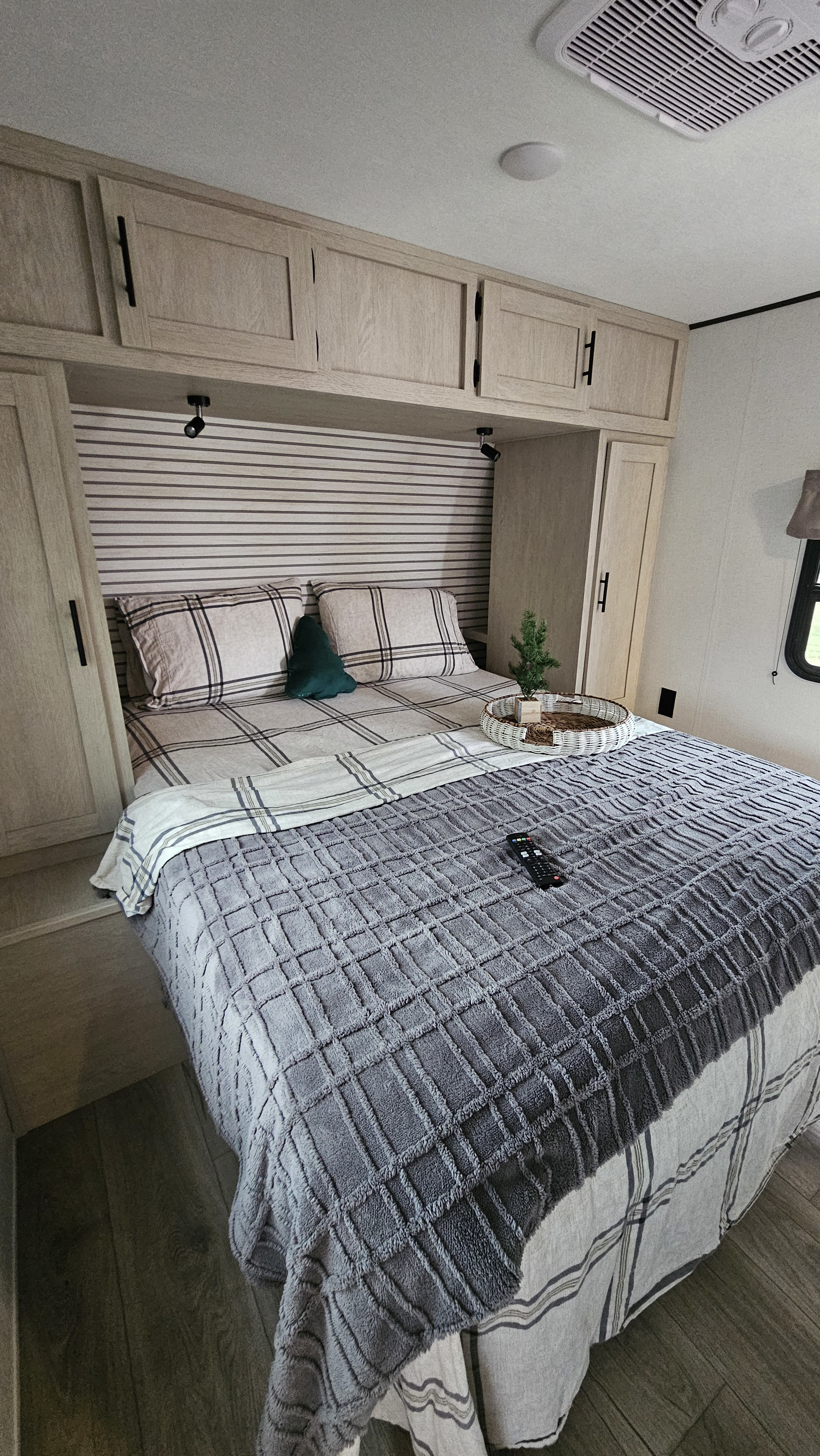 This inviting RV rental bedroom features a comfy bed with plaid and textured blankets, built-in cabinets, and ceiling AC.. Forest River Shasta I-5 2025