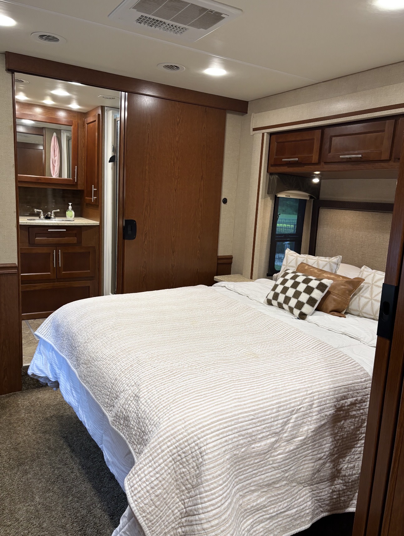 Cozy RV rental bedroom featuring a striped bed, decorative pillows, and an attached compact bathroom vanity.. Berkshire Berkshire Motorhome 2015