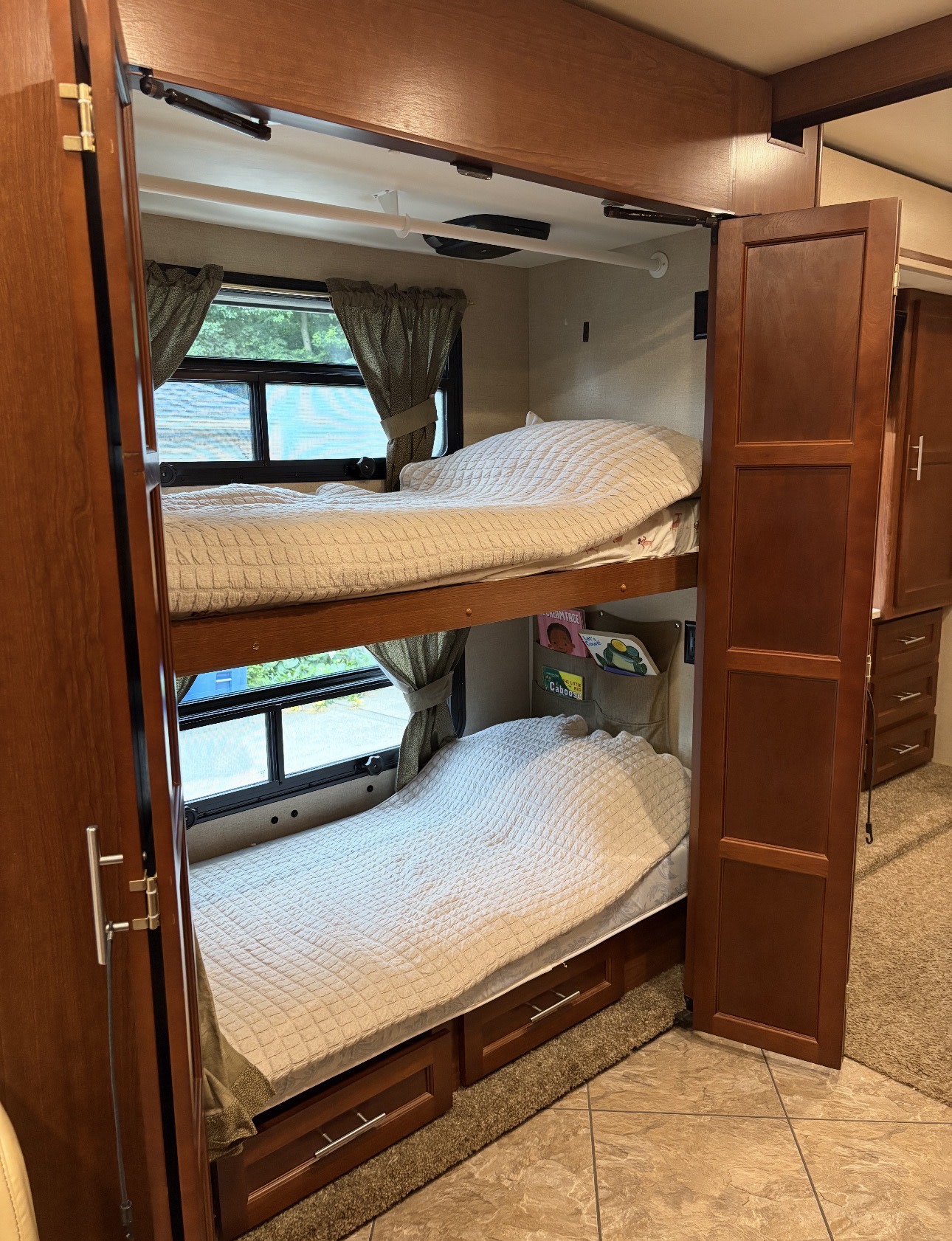 Cozy bunk beds inside an RV rental, featuring two beds with windows, quilted comforters, and storage drawers.. Berkshire Berkshire Motorhome 2015