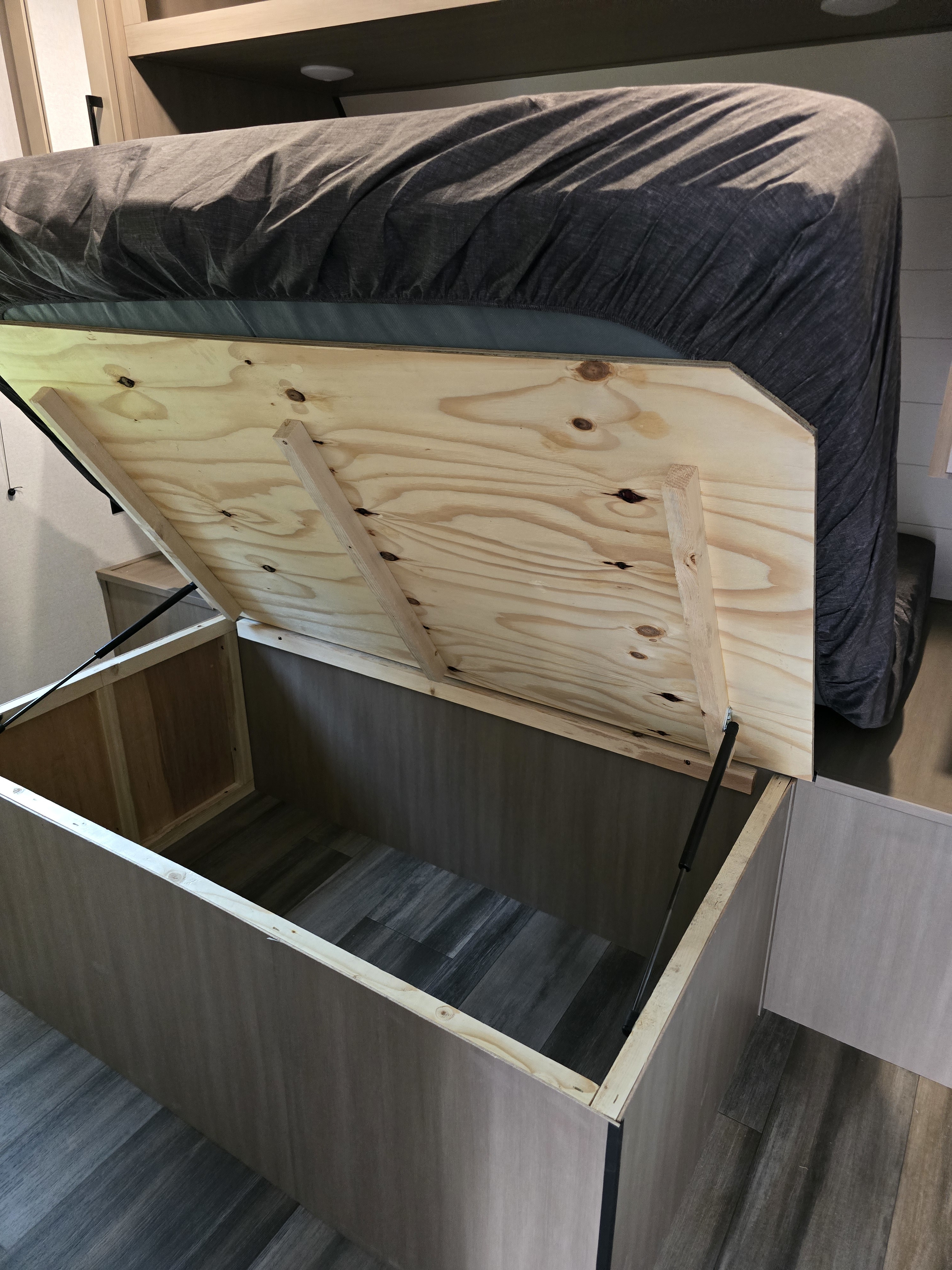 RV rental bed lifted, showing plywood base and deep under-bed storage compartment held open by gas struts.. Highland Ridge RV Colt 2026
