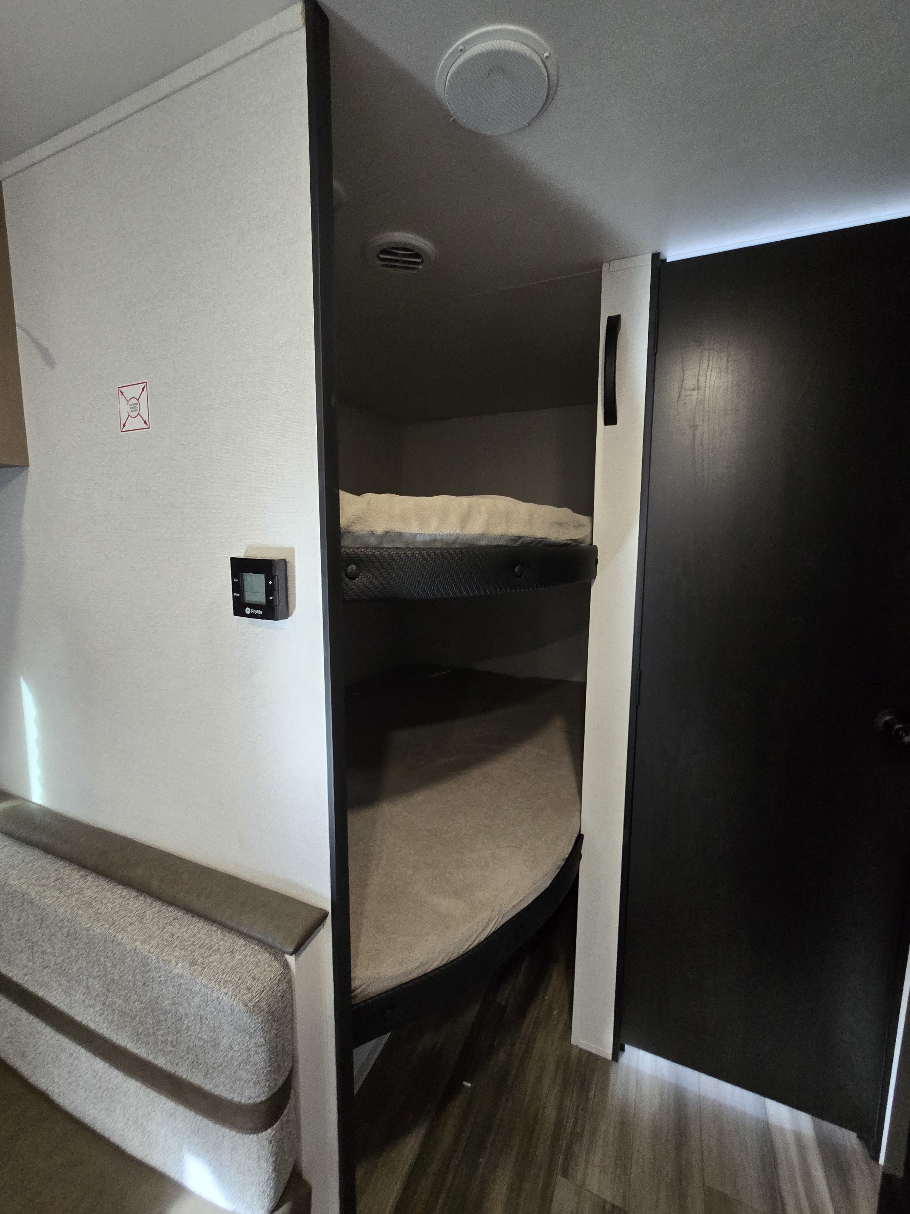 Inside an rv rental: cozy bunk beds, a thermostat on the wall, and a dark door, offering comfortable sleeping arrangements.. Highland Ridge RV Colt 2026