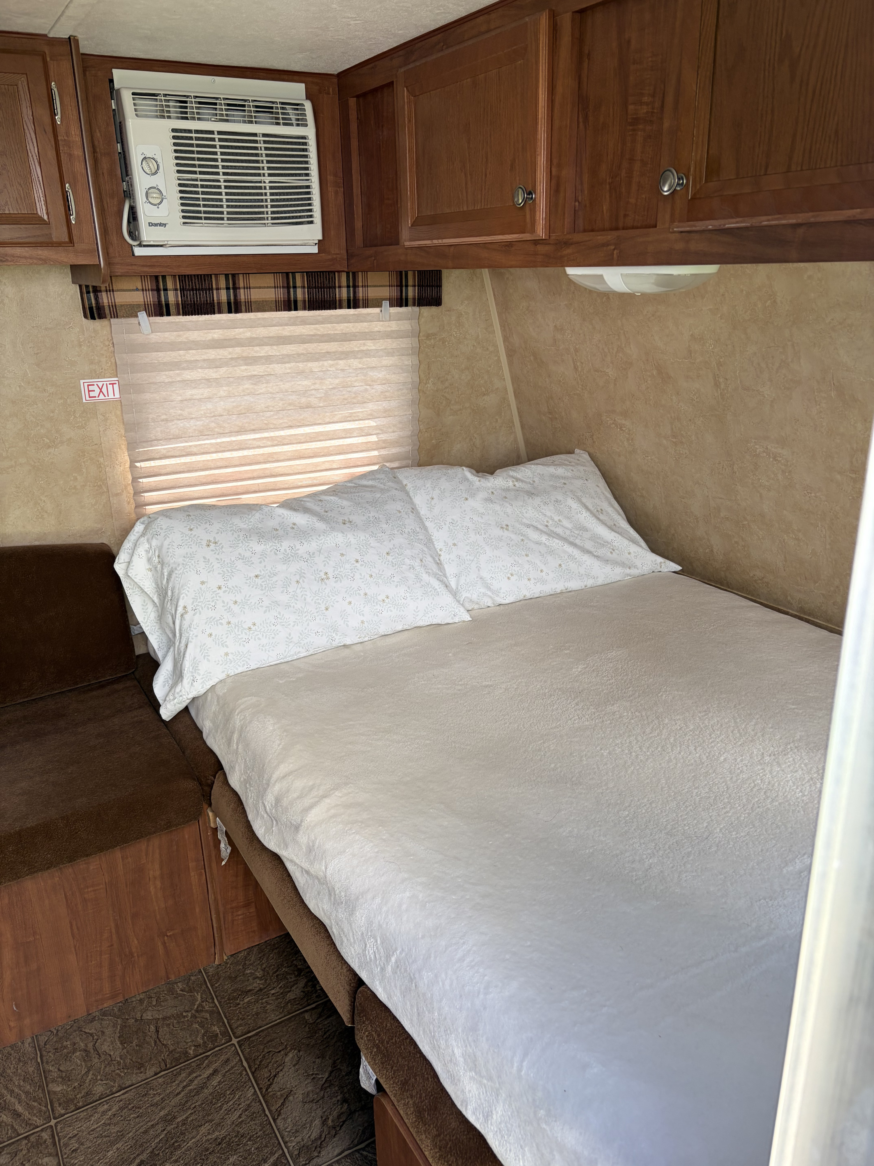 This cozy RV rental bedroom features a comfortable bed, pillows, an AC unit, overhead cabinets, and an exit sign.. Jayco Jay Flight Swift SLX 2012