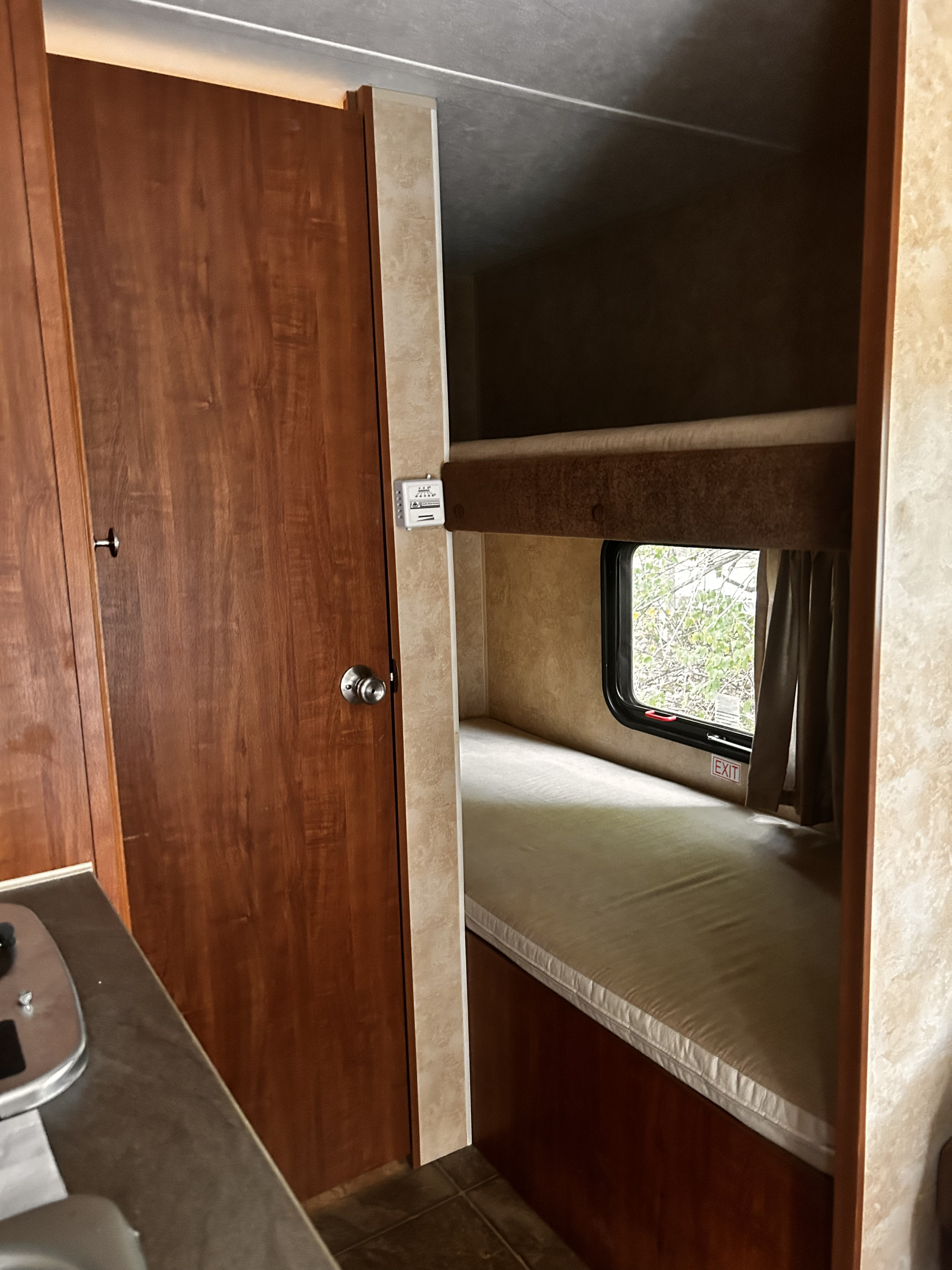 This RV rental's cozy interior features bunk beds with mattresses, a window, exit sign, thermostat, and a wooden door.. Jayco Jay Flight Swift SLX 2012