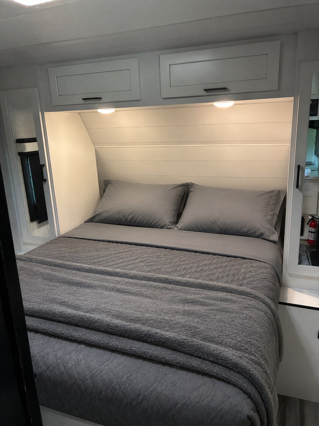 This RV rental offers a cozy, modern bedroom with a gray bed, overhead cabinets, and lighting for a relaxing stay.. Jayco Jay Feather 2024