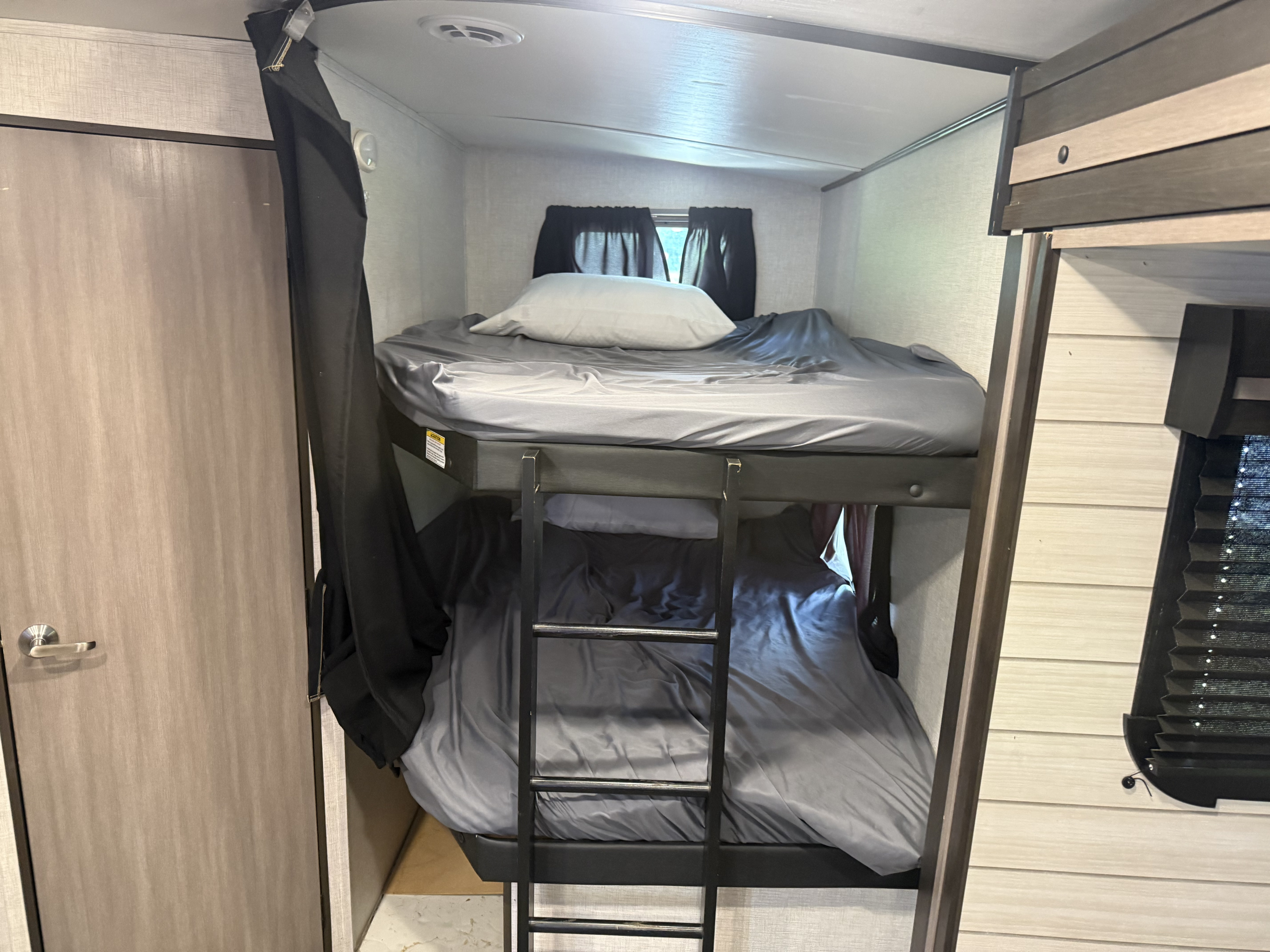 An RV rental provides cozy bunk beds with grey sheets, a ladder, and privacy curtains, perfect for family travel.. Crossroads RV Sunset Trail Super Lite 2022