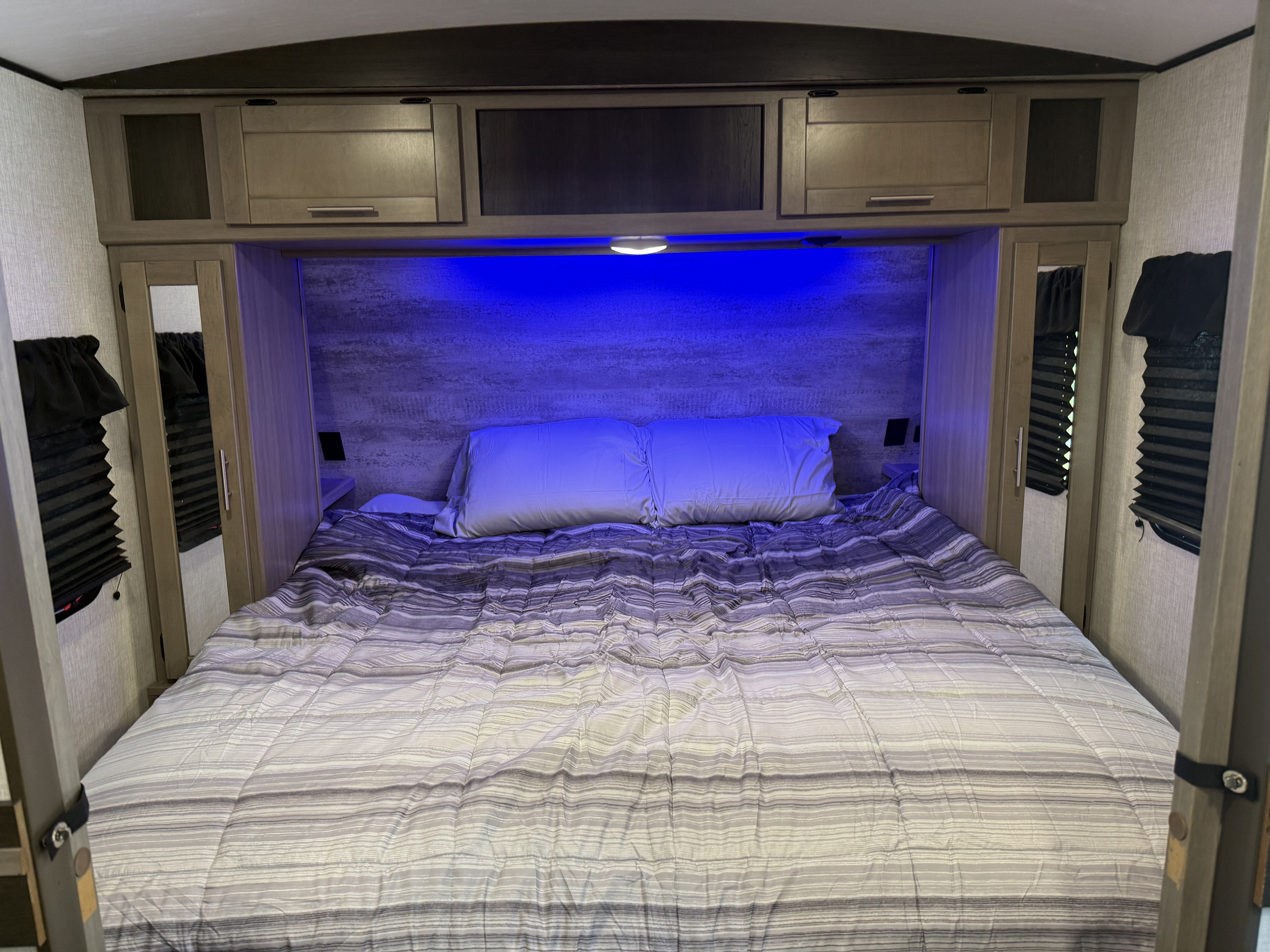 Cozy RV rental bedroom featuring a queen bed, ambient blue lighting, built-in storage, and side wardrobes.. Crossroads RV Sunset Trail Super Lite 2022