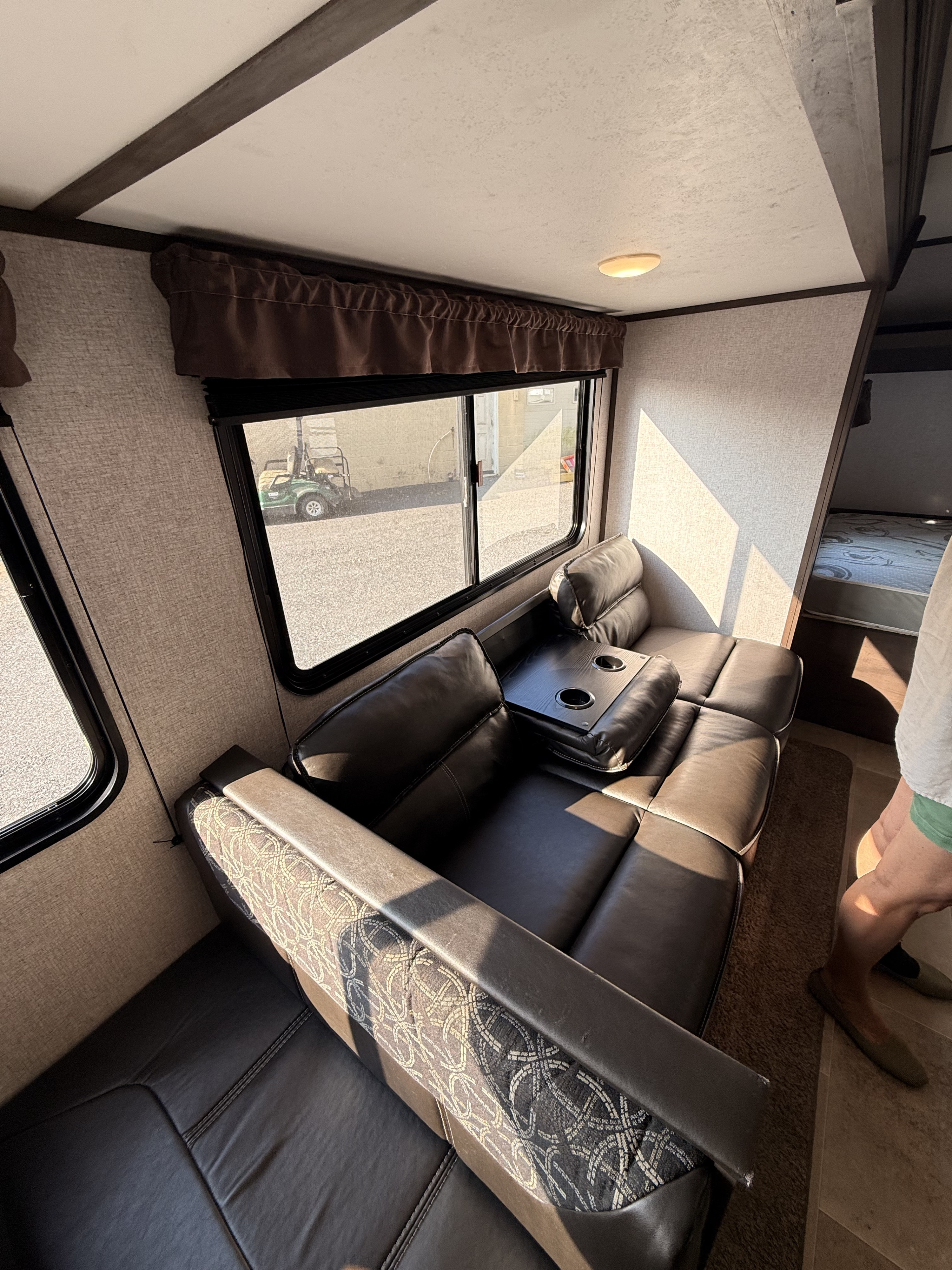 RV rental interior: Comfortable dark sofa with cup holders, patterned armrests, bright windows, and a glimpse of the bedroom.. Dutchmen Coleman Lantern LT 2021