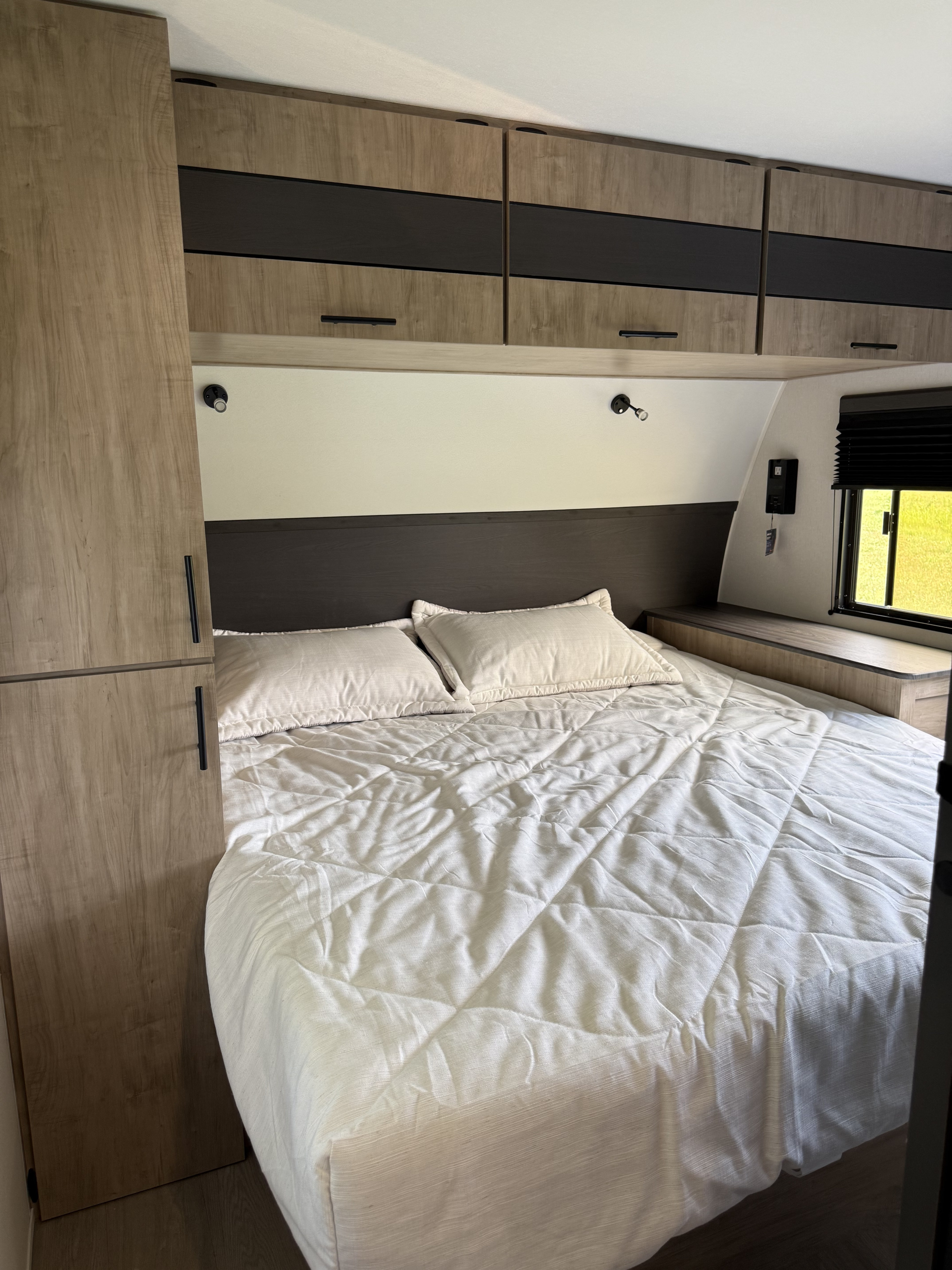 An inviting RV rental bedroom featuring a comfortable bed, modern cabinets, bedside lighting, and a scenic window view.. Forest river Campsite Reserve 26cj 2027