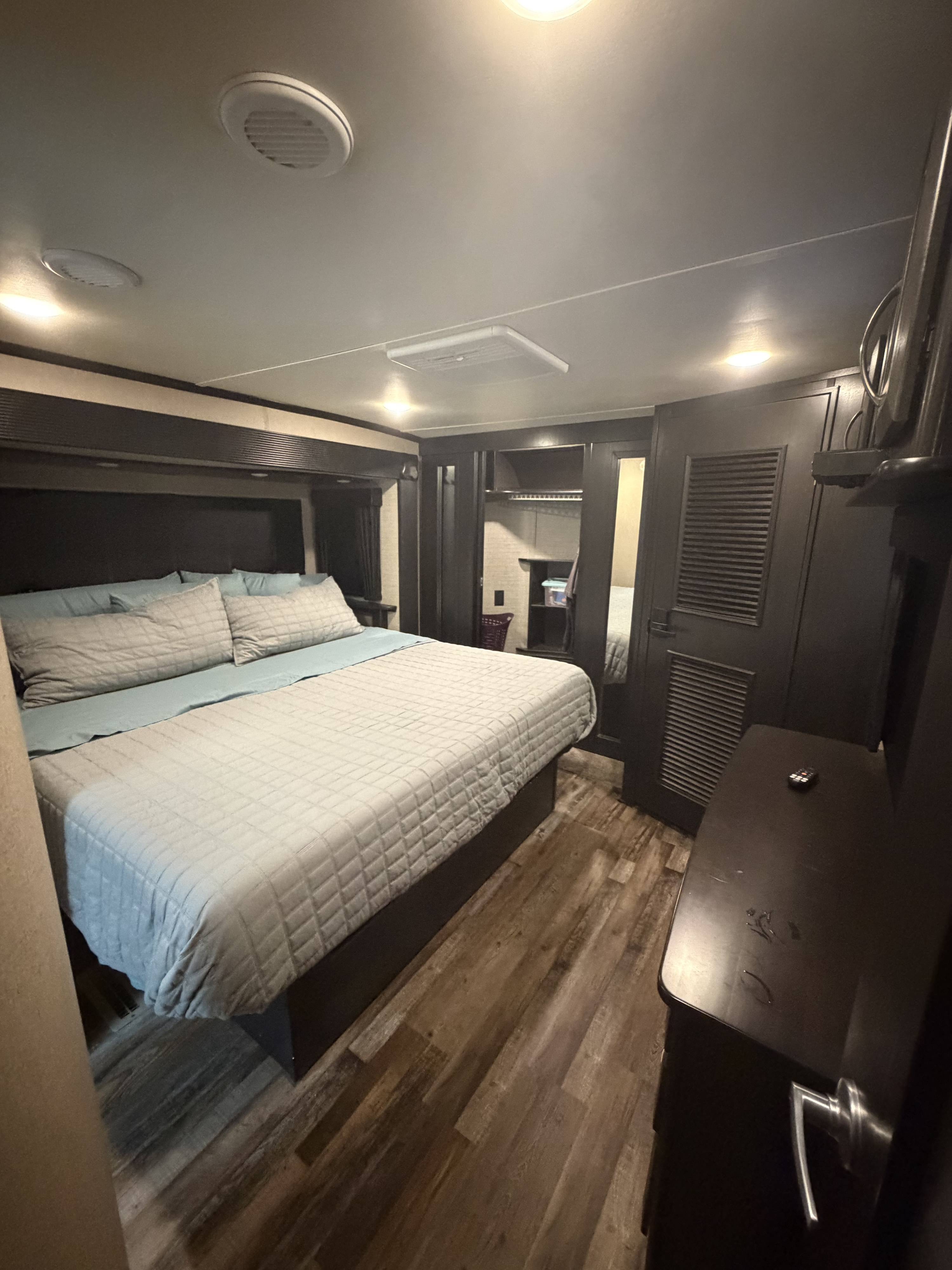 An inviting RV rental bedroom with a large bed, light blue bedding, and dark wood cabinetry. Wood-look floors complete the modern interior.. Denali Denali Fifth Wheel 2017