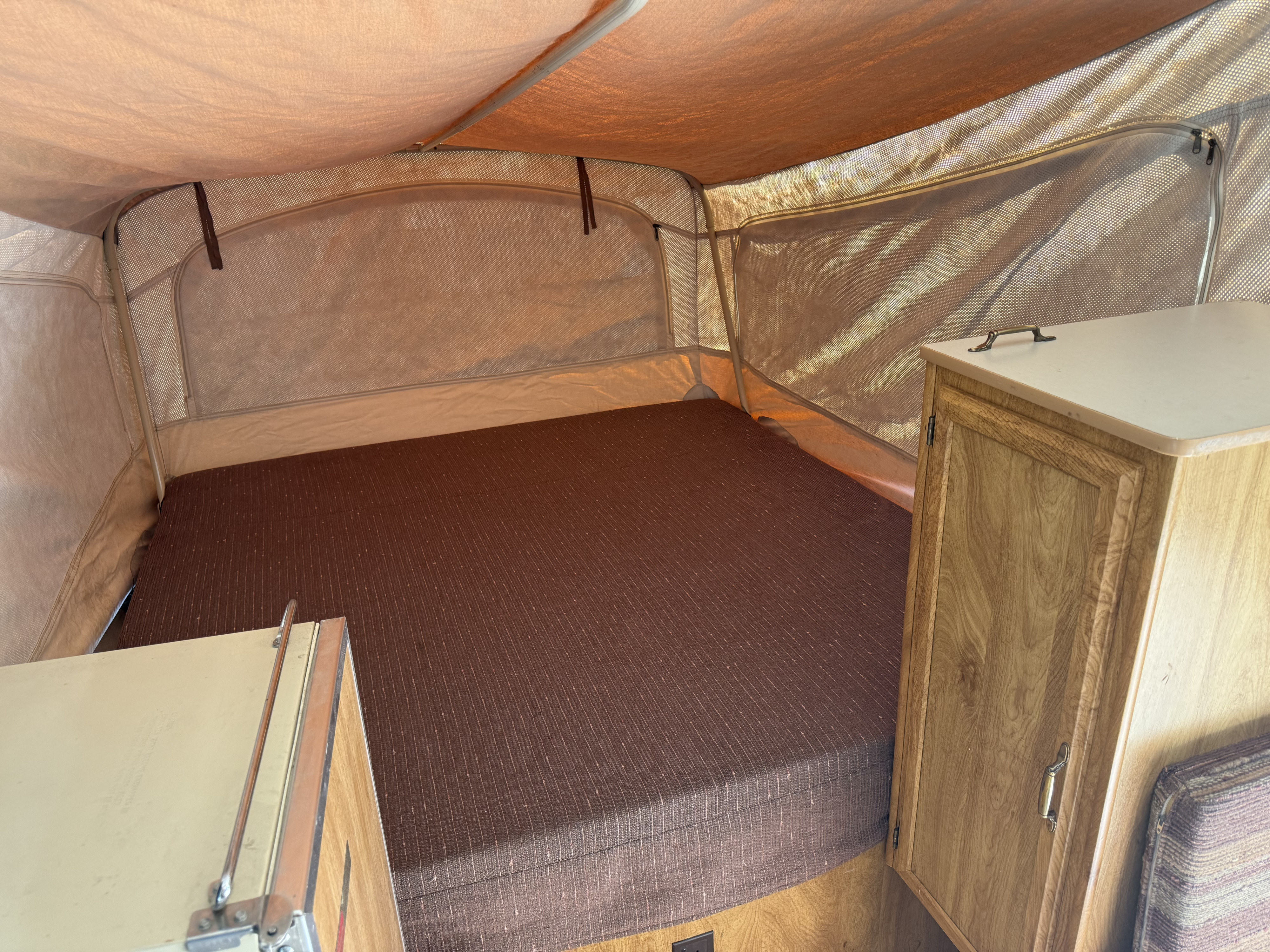 RV rental interior showing a pop-up camper bed, mesh windows, and wooden cabinetry.. Coleman Grand Tour Shenandoah 1987