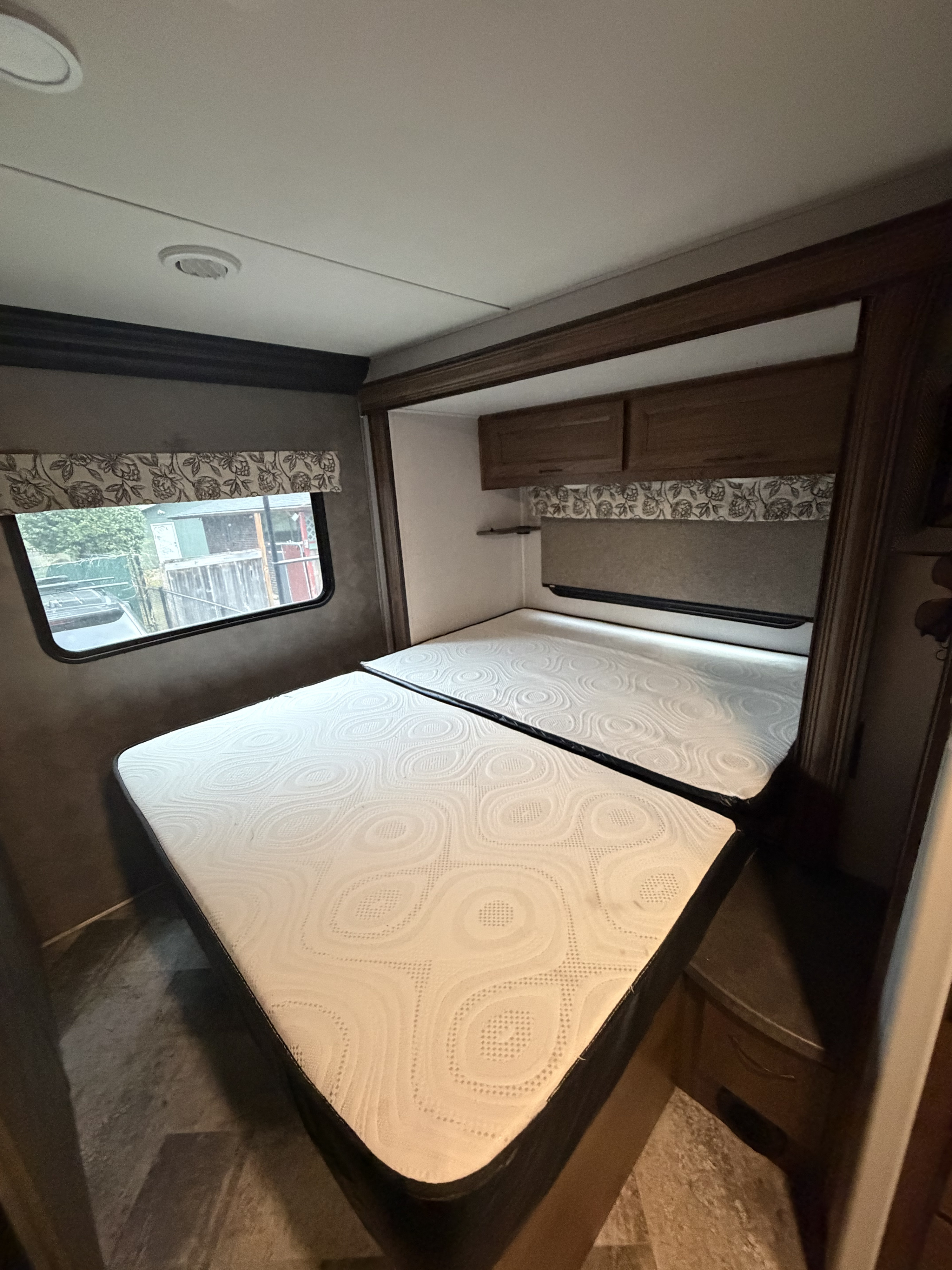 Inside an RV rental: A bedroom with two white mattresses, a window to the left, and wooden overhead cabinets.. Forester LE 2020