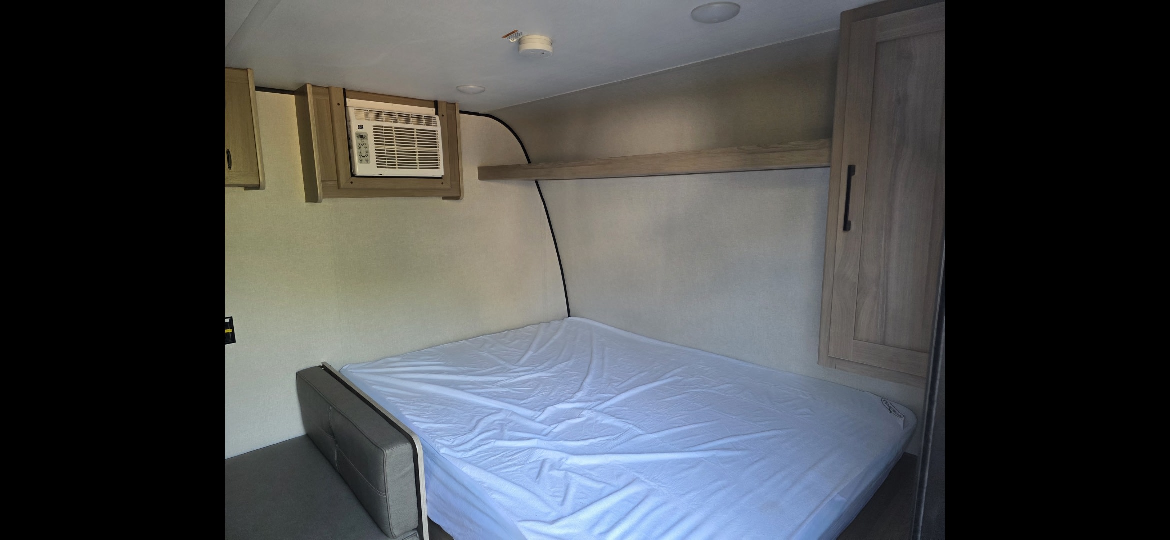 RV rental bedroom with a comfy bed, wall-mounted AC unit, overhead shelf, and storage cabinets. Ready for your adventure.. Keystone RV Coleman 2025
