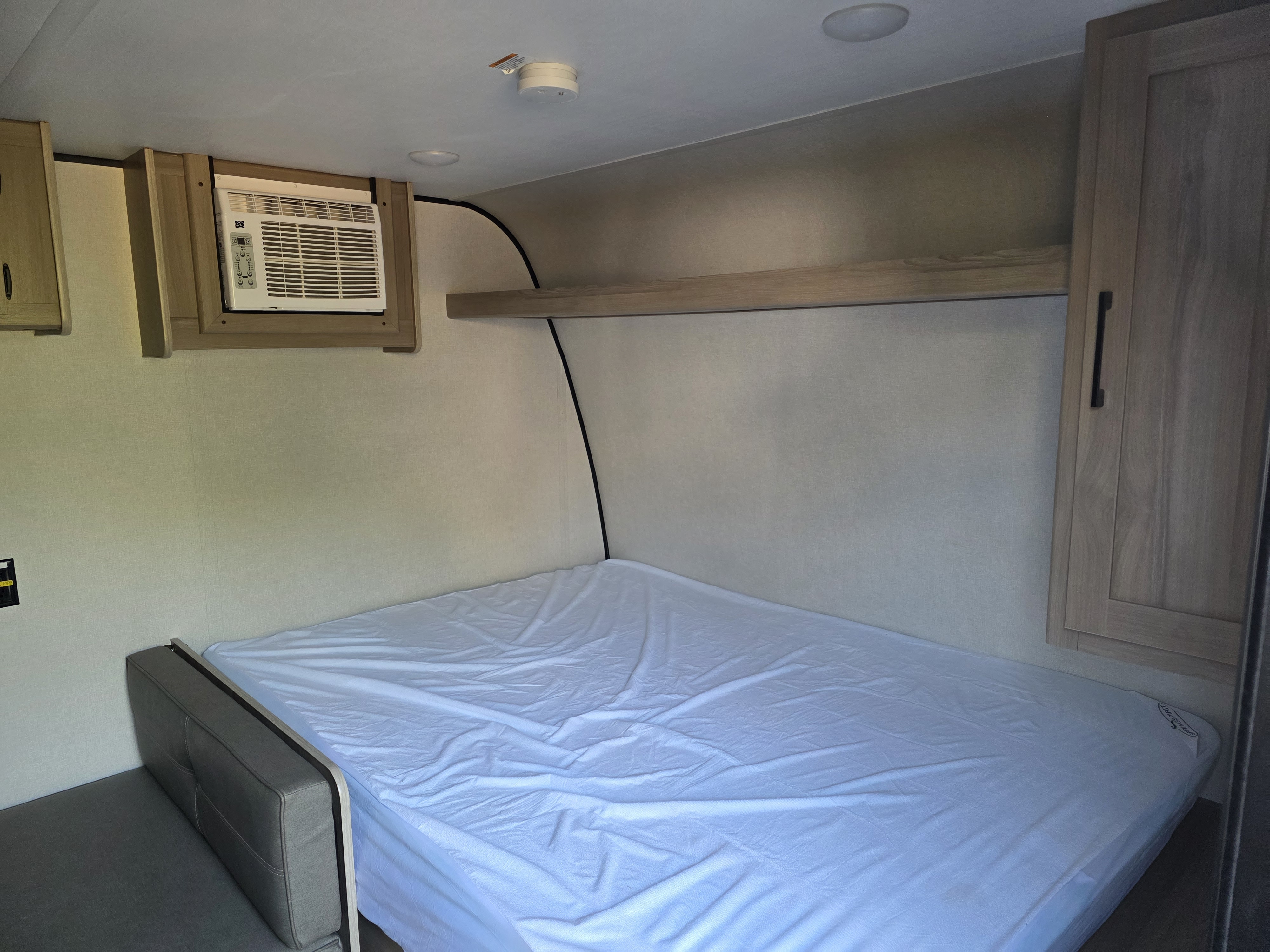 This rv rental bedroom features a comfy bed with a white sheet, wall-mounted AC, and built-in storage.. Keystone RV Coleman 2025