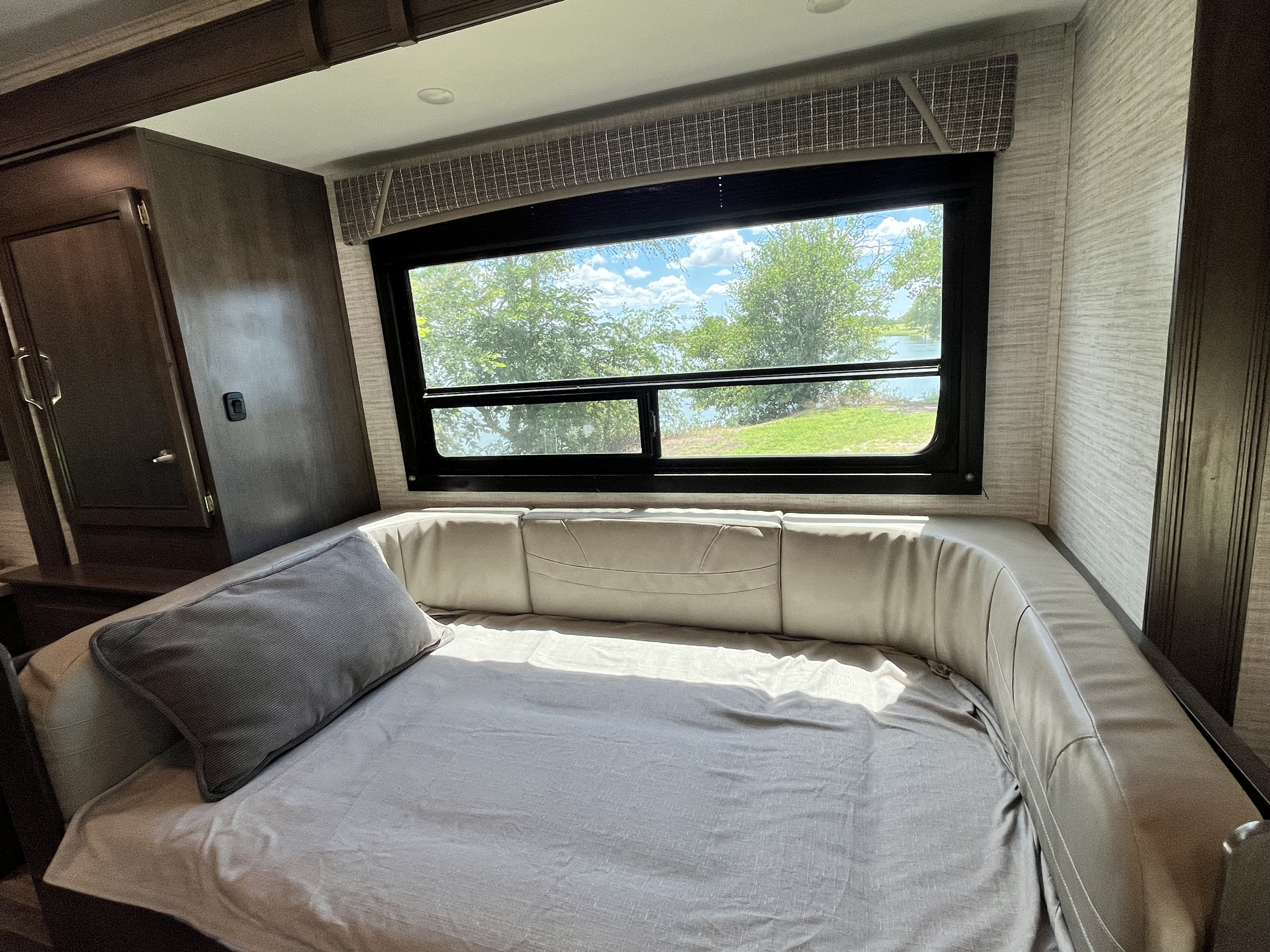Cozy RV rental bed with a large window showcasing a beautiful nature view of a lake and surrounding trees.. Jayco Redhawk SE 2024