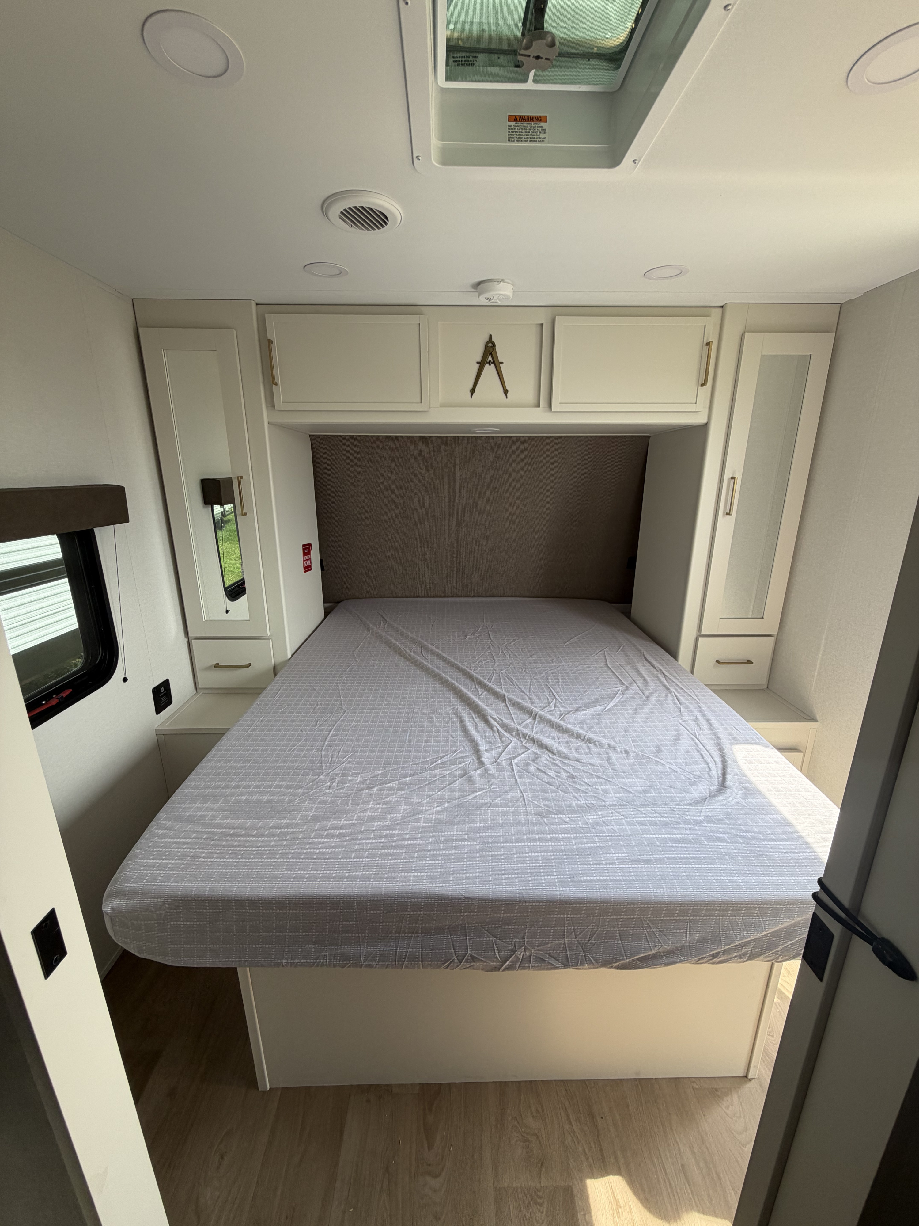 This inviting RV rental bedroom features a comfortable bed, integrated storage cabinets, and a skylight, perfect for travel.. Grand design Transcend 2027