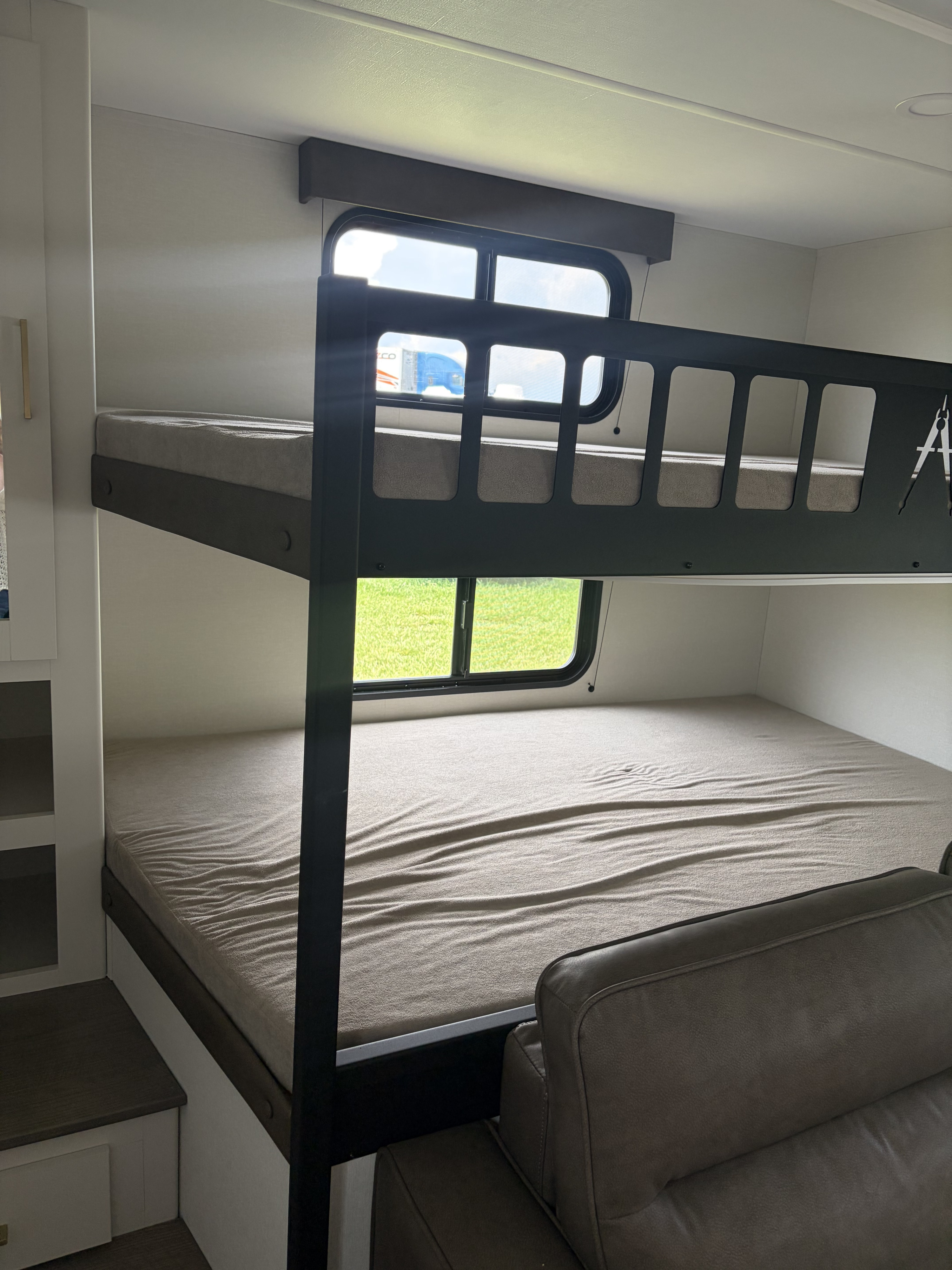 Bunk beds in this bright rv rental offer sleeping space & window views. Mattresses visible, with a sofa nearby. Ideal for families.. Grand design Transcend 2027
