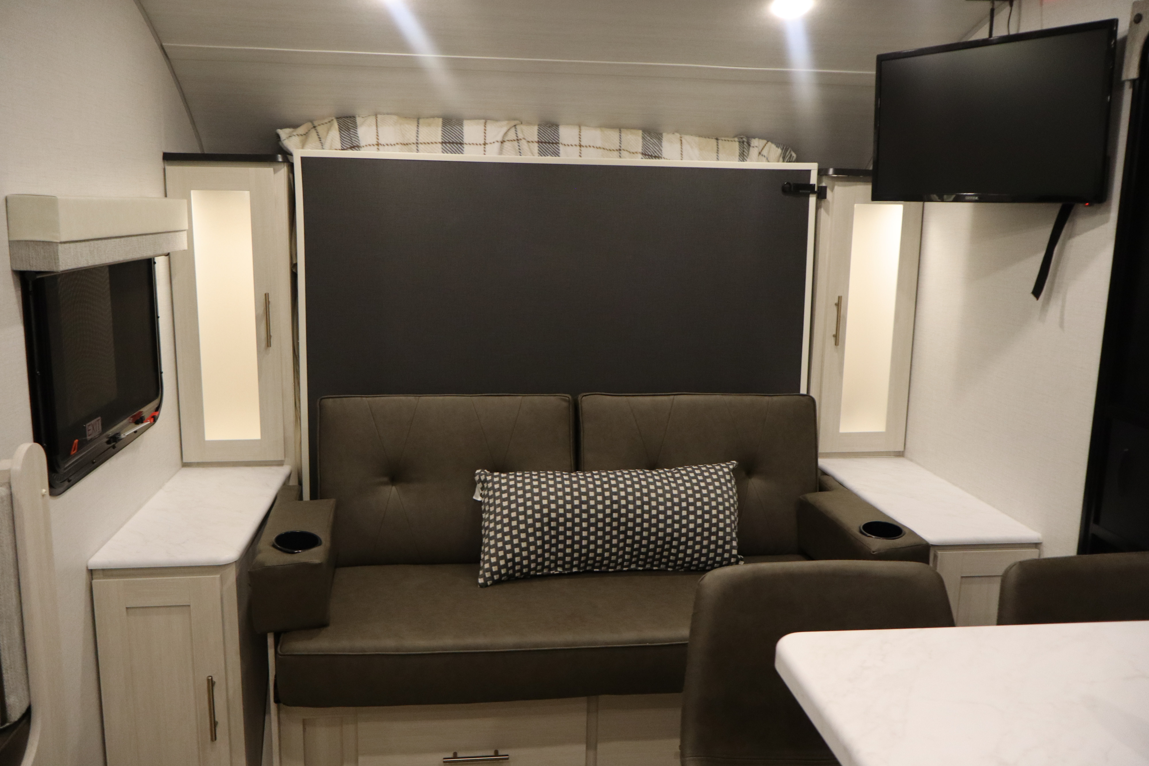 Compact rv rental interior with a cozy sofa, TV, and storage. A large dark panel behind the couch maximizes space.. R-Pod R-Pod Trailer 2026