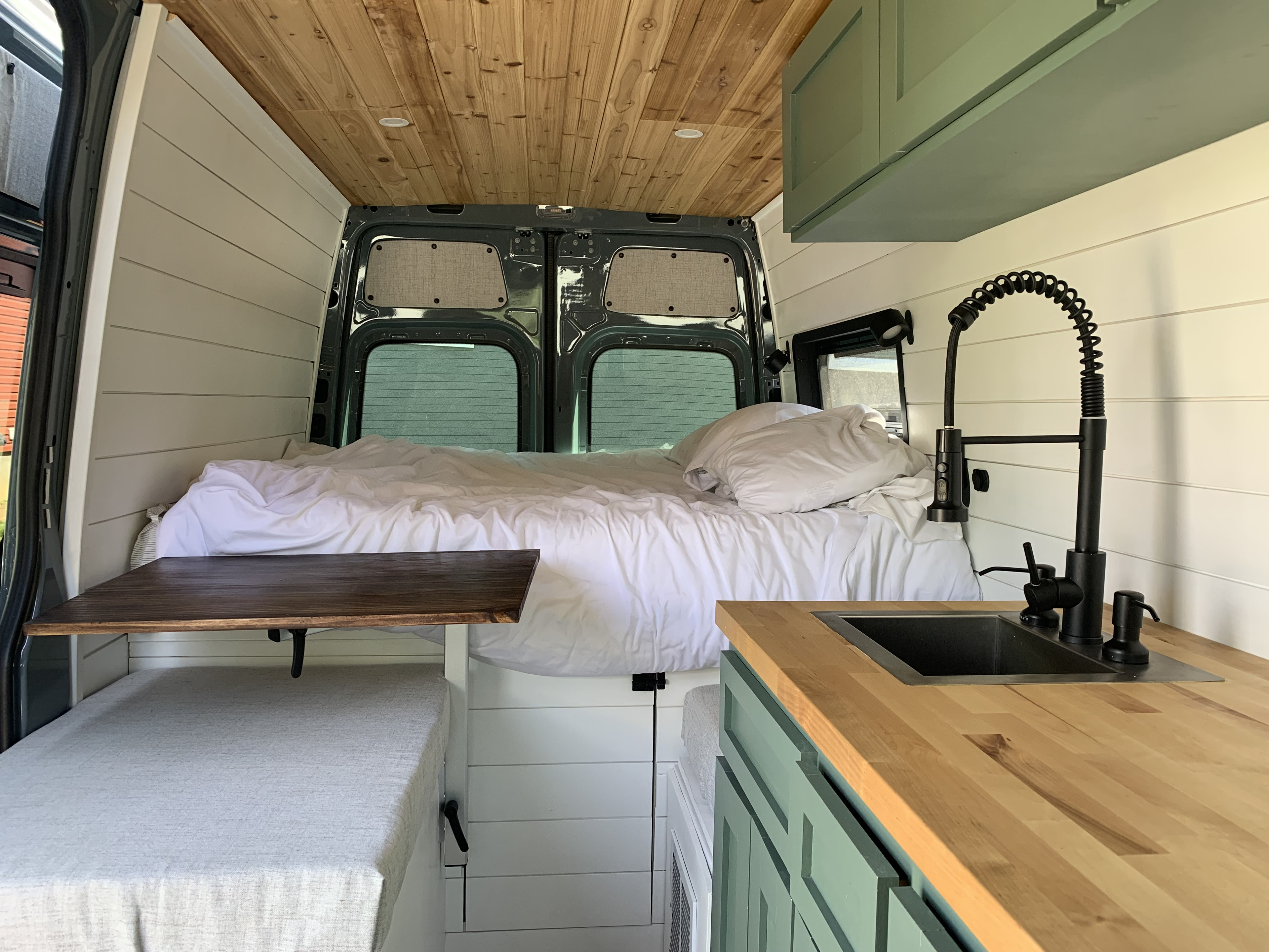 Stylish rv rental camper van interior featuring a comfortable bed, kitchen, wood ceiling, and pull-out table.. Mercedes-Benz Sprinter 2021