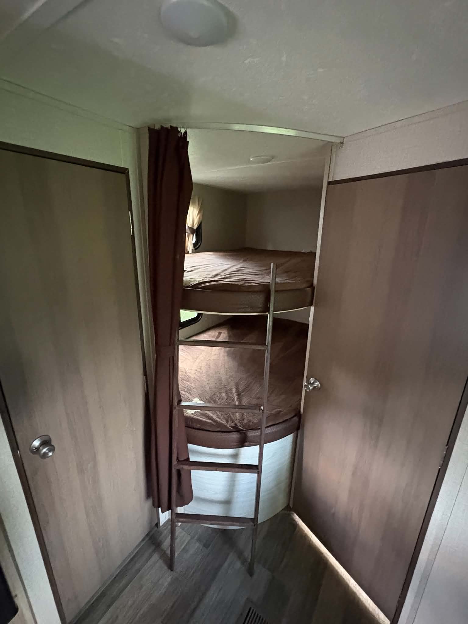 Inside an RV rental: two bunk beds with brown bedding and a metal ladder, flanked by wood-paneled doors and curtains.. Coachmen Catalina Summit 261bhs 2021