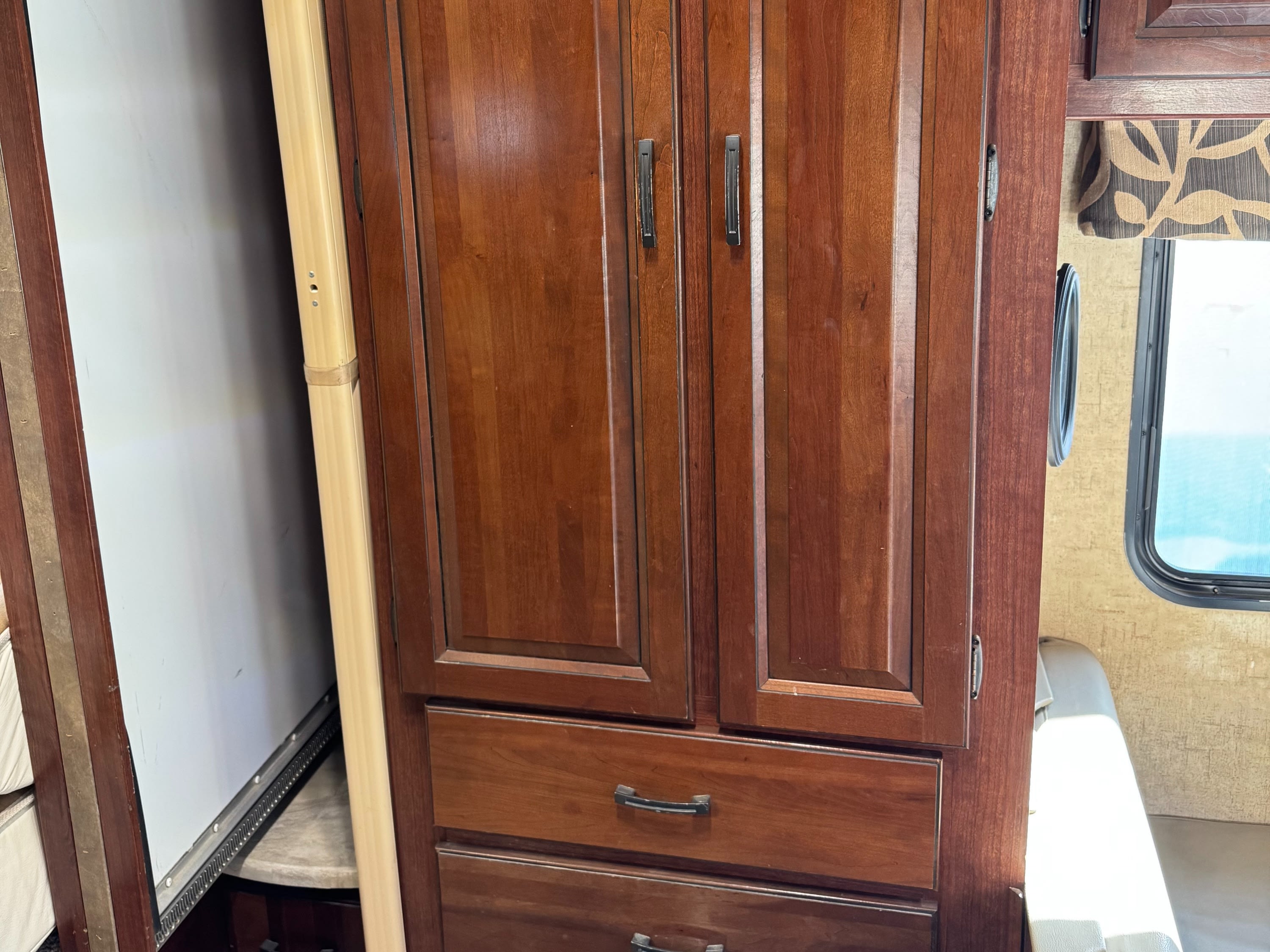RV rental interior: Detailed dark wood storage cabinets with drawers, adjacent to a beige slide-out expansion and a window.. Forester LE 2016