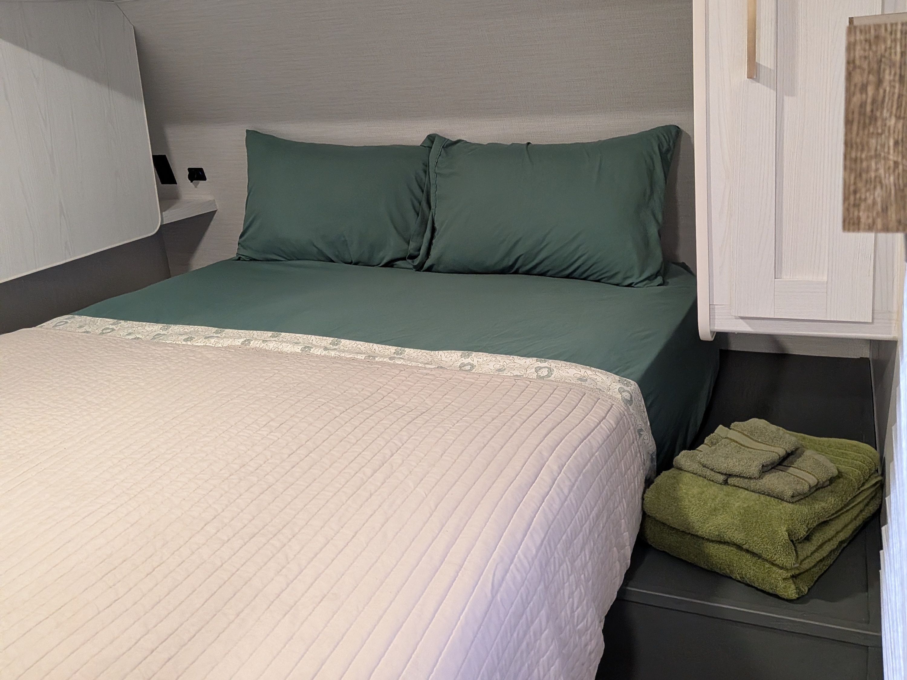 Comfortable RV rental bedroom featuring dark green bedding, a light quilted comforter, and green towels. Ideal for travel.. Eddie Bauer Eddie Bauer 2024