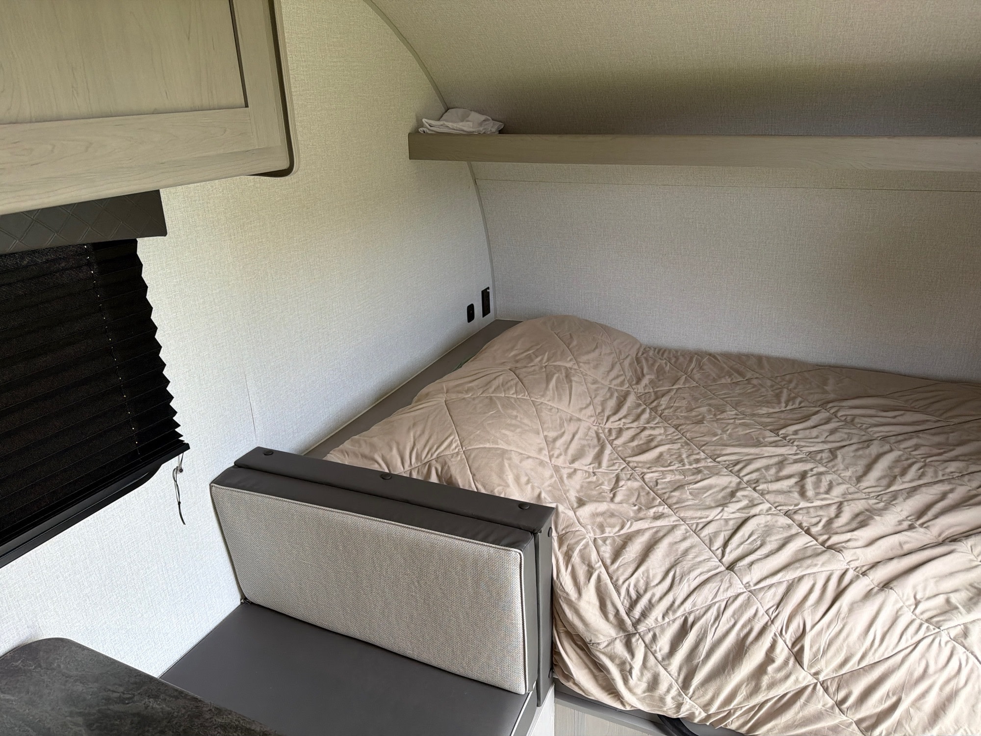 RV rental interior: cozy sleeping area with quilted bed, small dinette seating, window blind, and overhead shelf.. Coachmen Clipper 17BH 2024