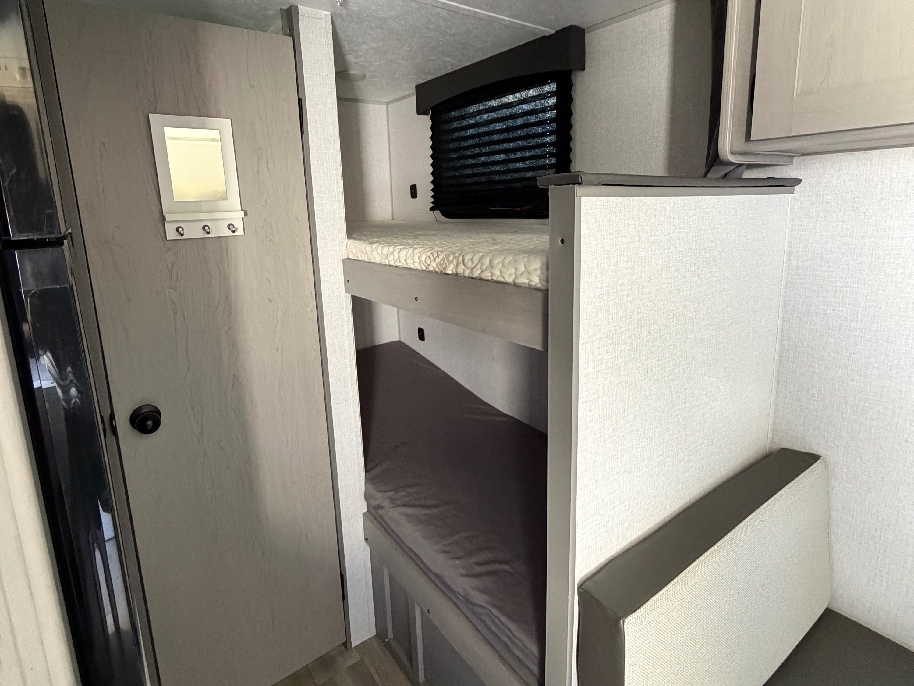 RV rental interior featuring bunk beds, a dinette seating area, and a door with a mirror. A compact, functional living space.. Coachmen Clipper 17BH 2024