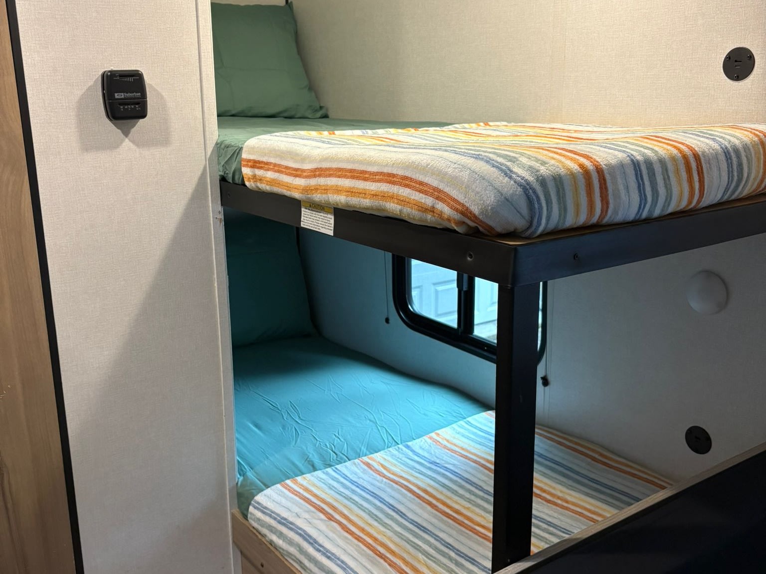 RV rental bunk beds in a compact sleeping area with striped blankets, window, thermostat, and USB charging ports.. Keystone RV Coleman 2025