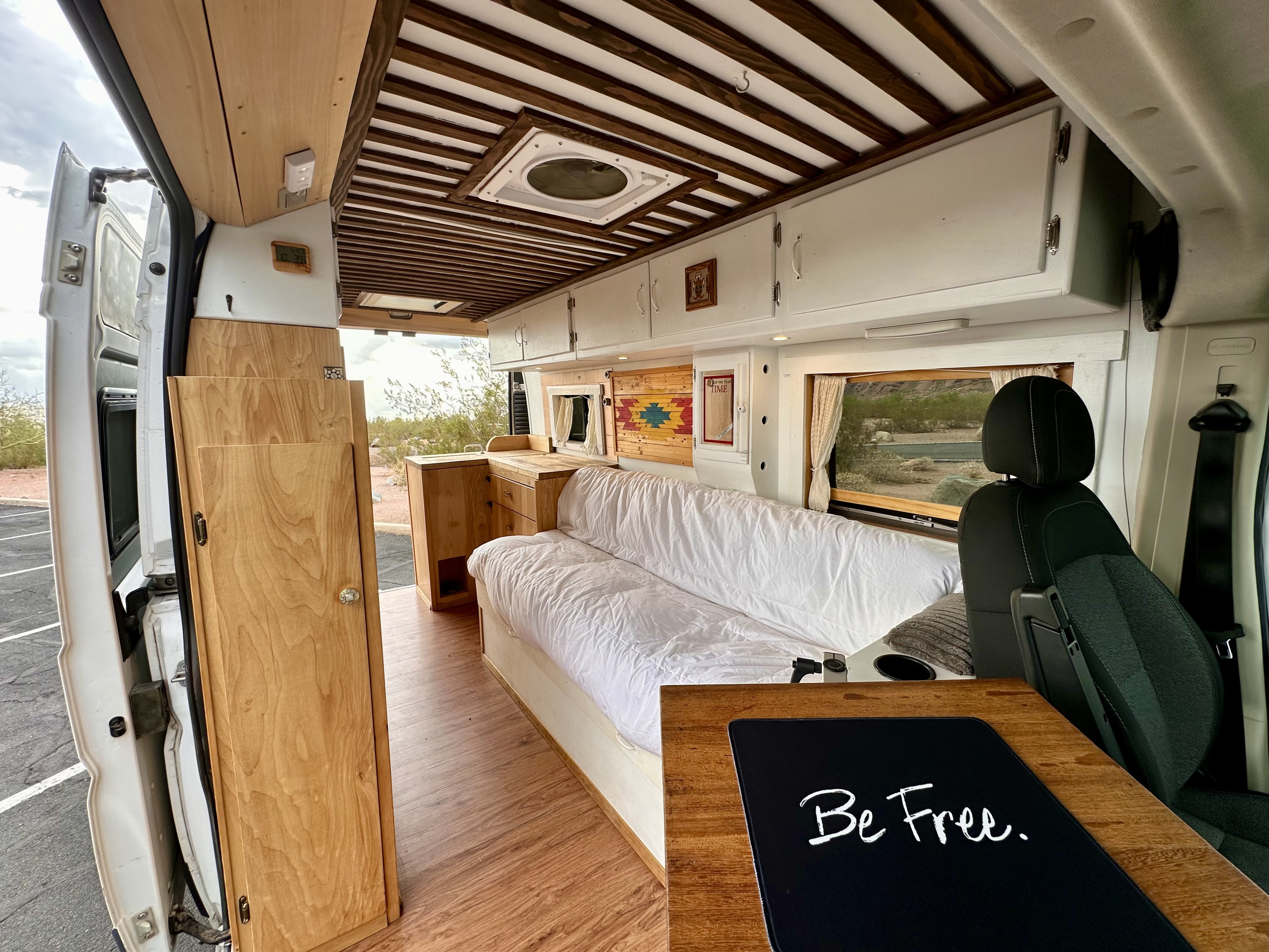 RV rental camper van interior. Features a comfy bed, kitchen, and wood details, perfect for mobile adventures and van life.. RAM Promaster 2018