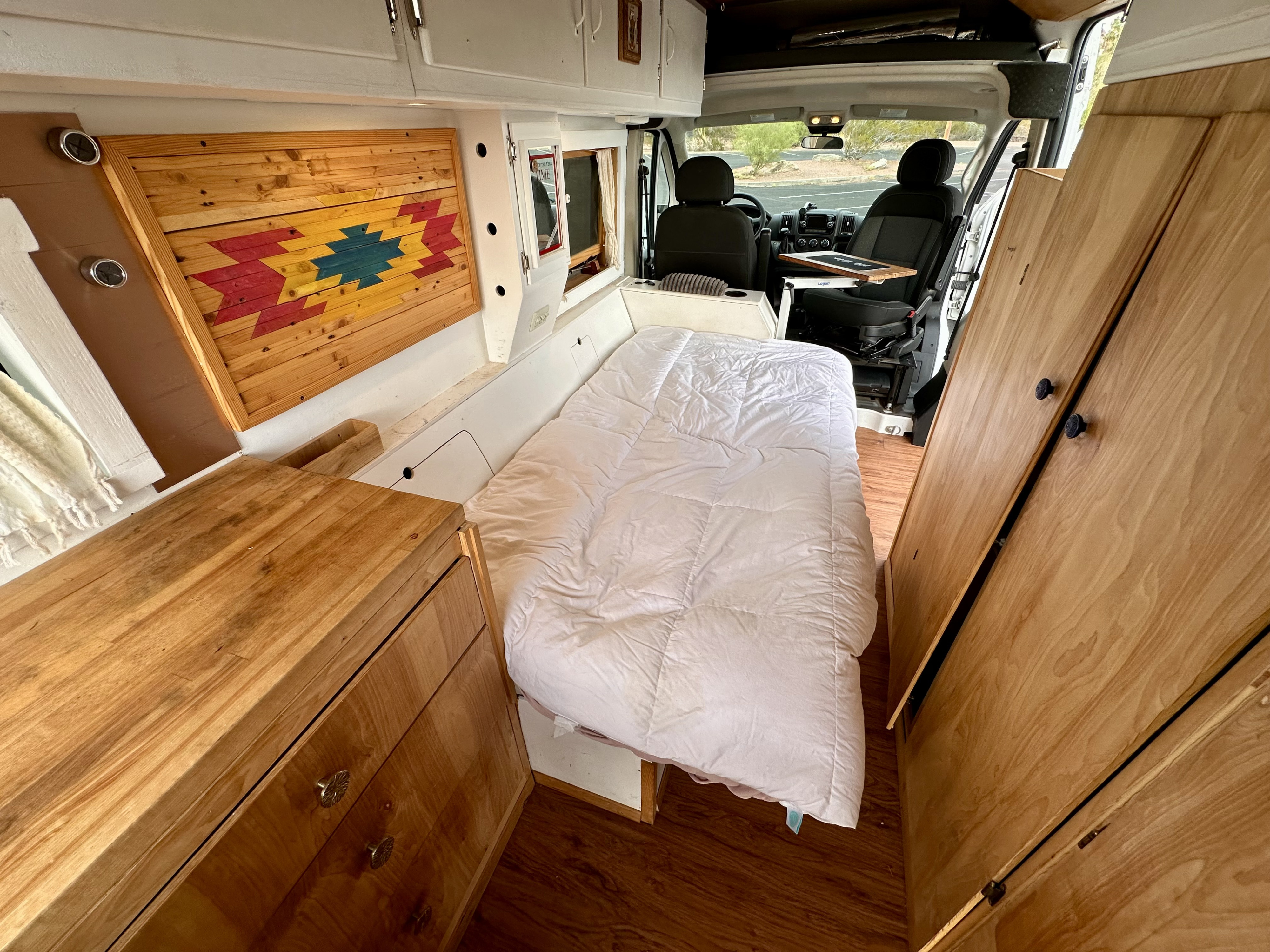 Cozy RV rental interior with bed, storage, and Southwestern decor. Perfect for road trip adventures and camper van travel.. RAM Promaster 2018