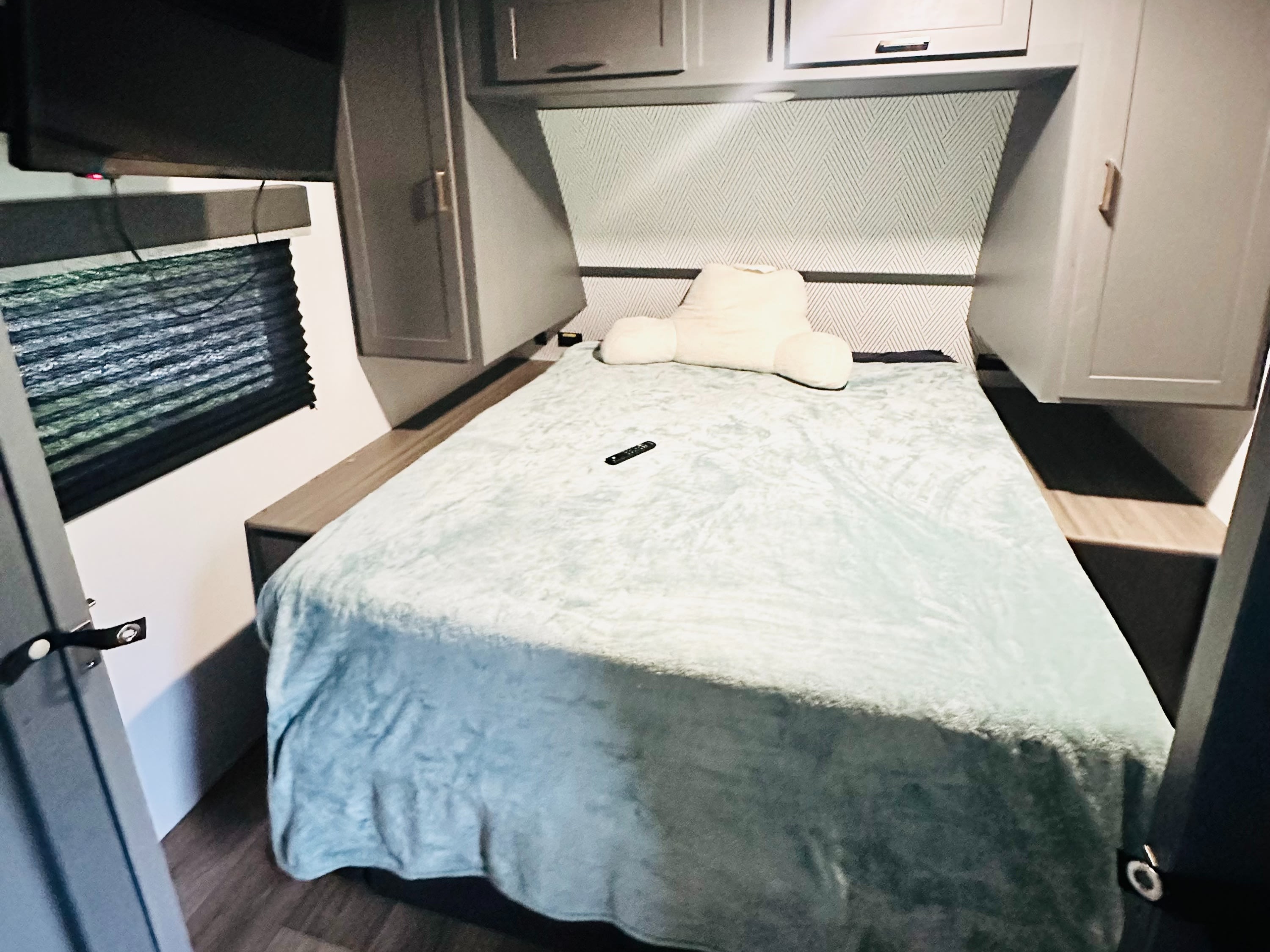 Cozy RV rental bedroom featuring a light blue bed, mounted TV, and practical overhead storage cabinets.. Keystone RV Bullet Crossfire 2024