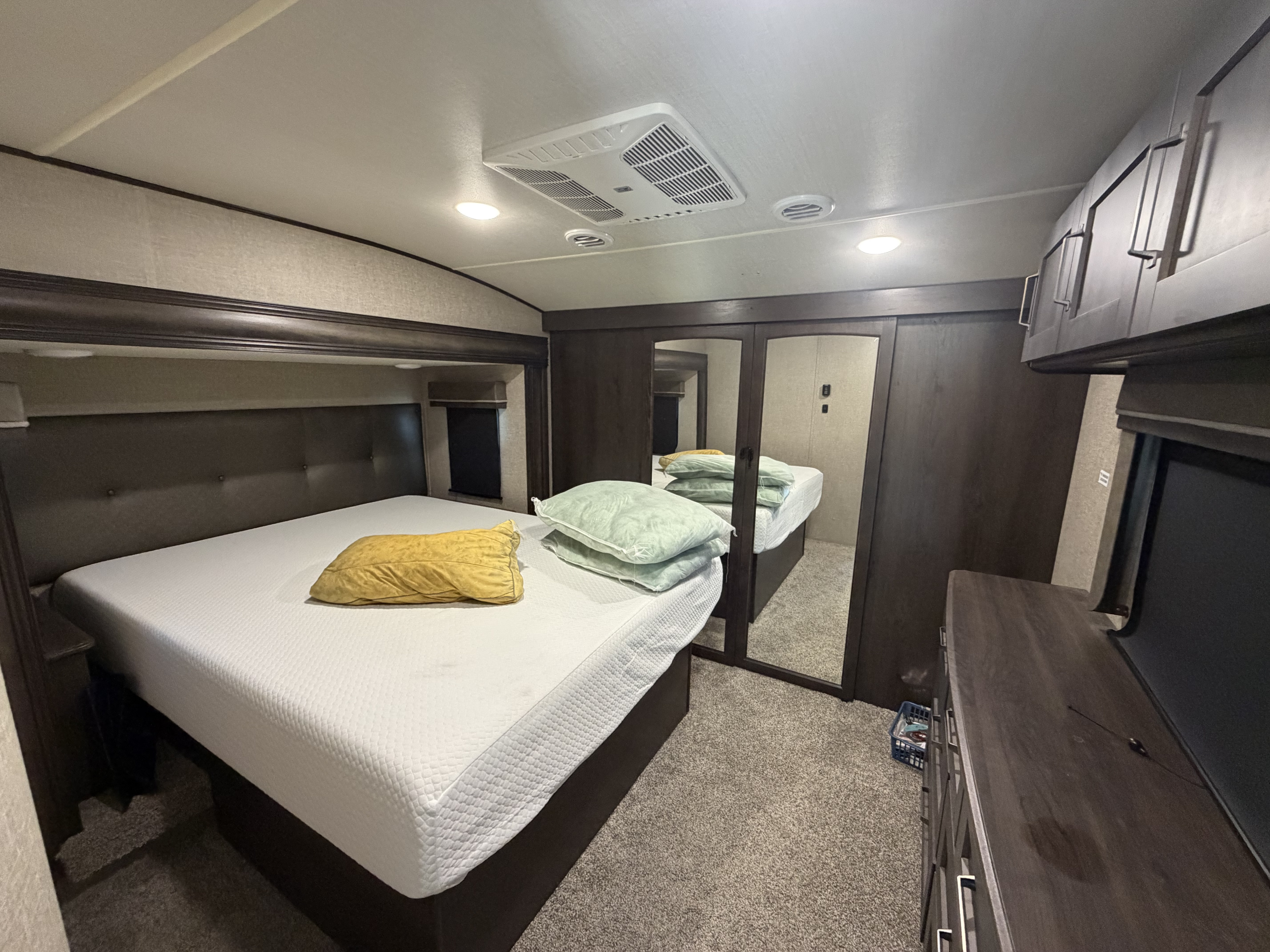 This RV rental features a comfortable bedroom with a queen bed, dark headboard, mirrored closet, and ceiling AC unit.. Grand Design Reflection 2023