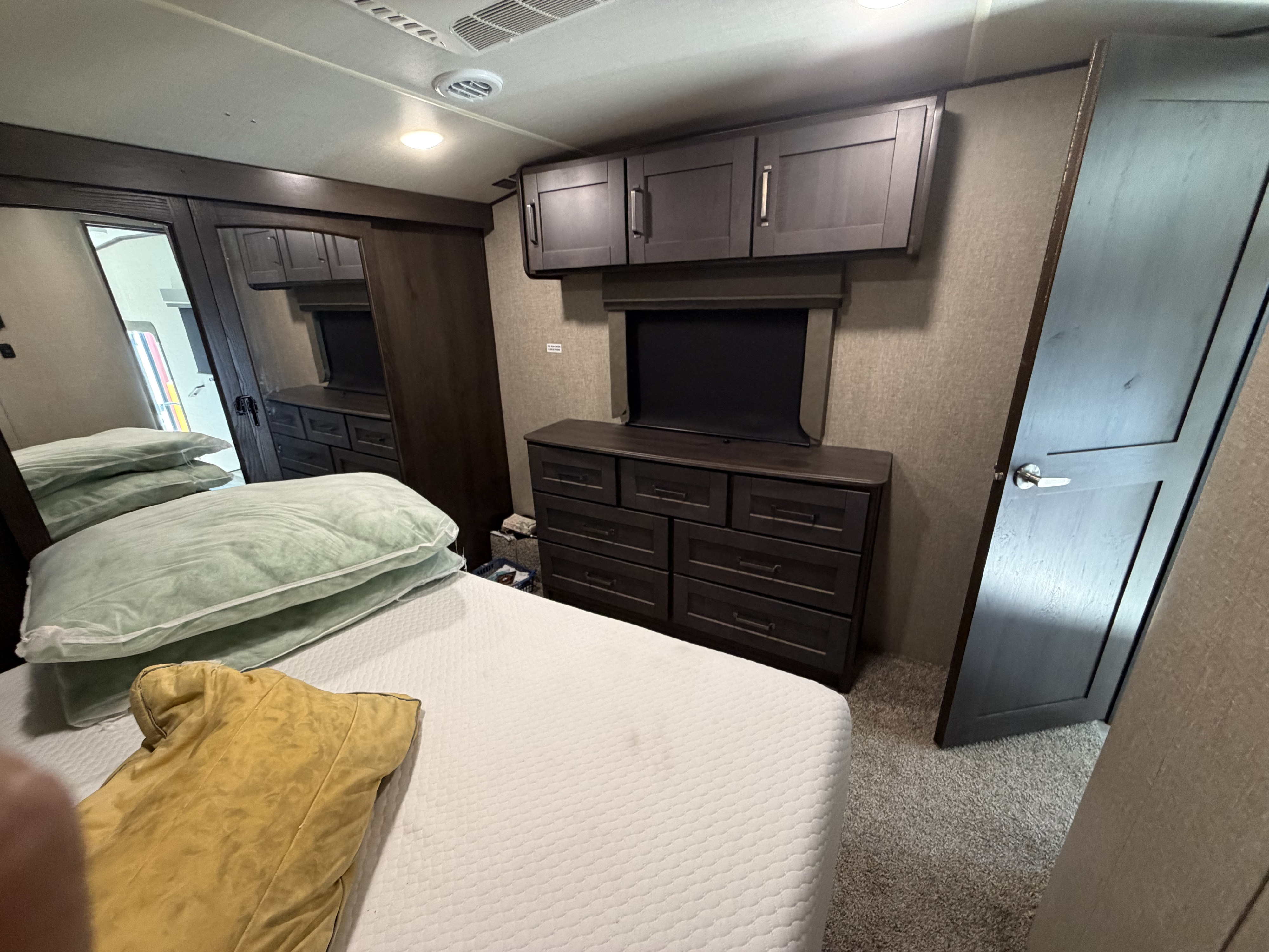 Inside an RV rental: a cozy bedroom with a bed, dark wood dresser, cabinets, and a mirrored closet, offering comfort on the go.. Grand Design Reflection 2023