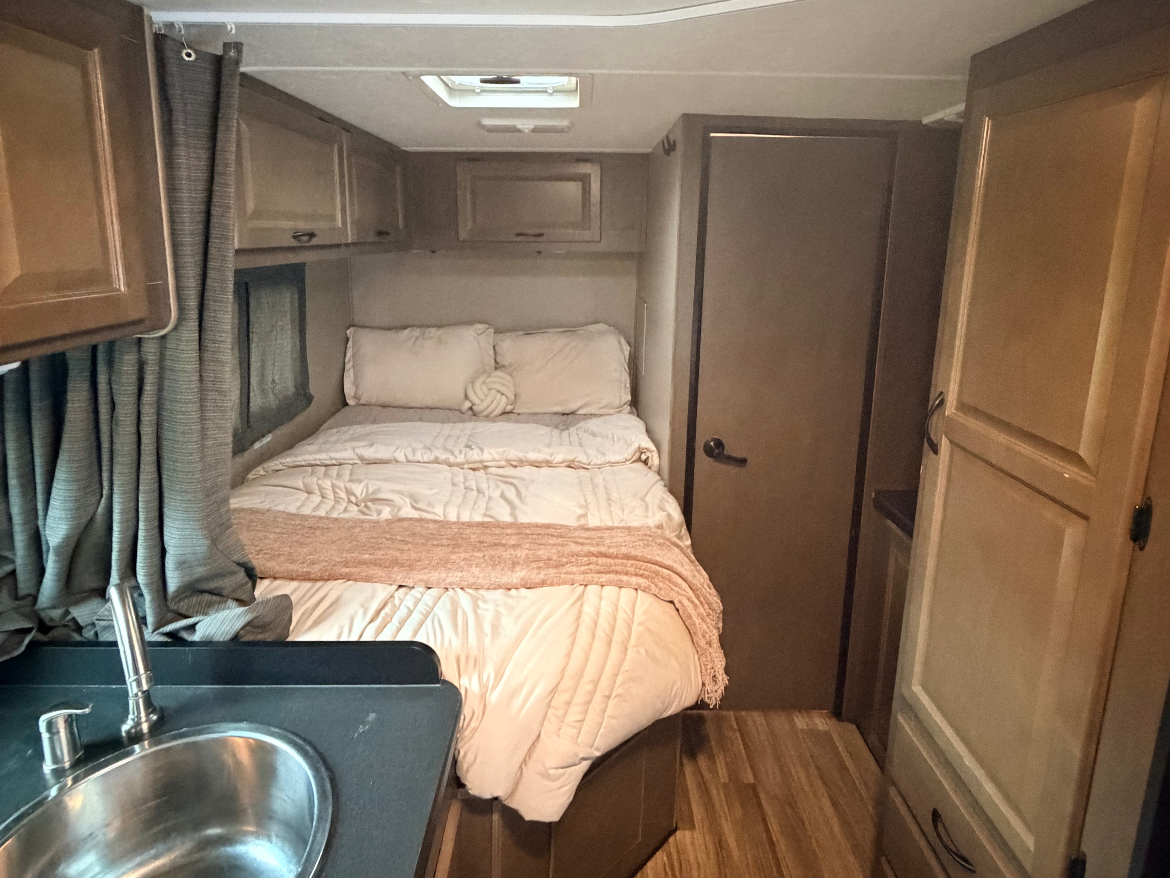 RV rental bedroom with cozy bed, light bedding, overhead cabinets, and a small sink area visible.. Thor Majestic 2019