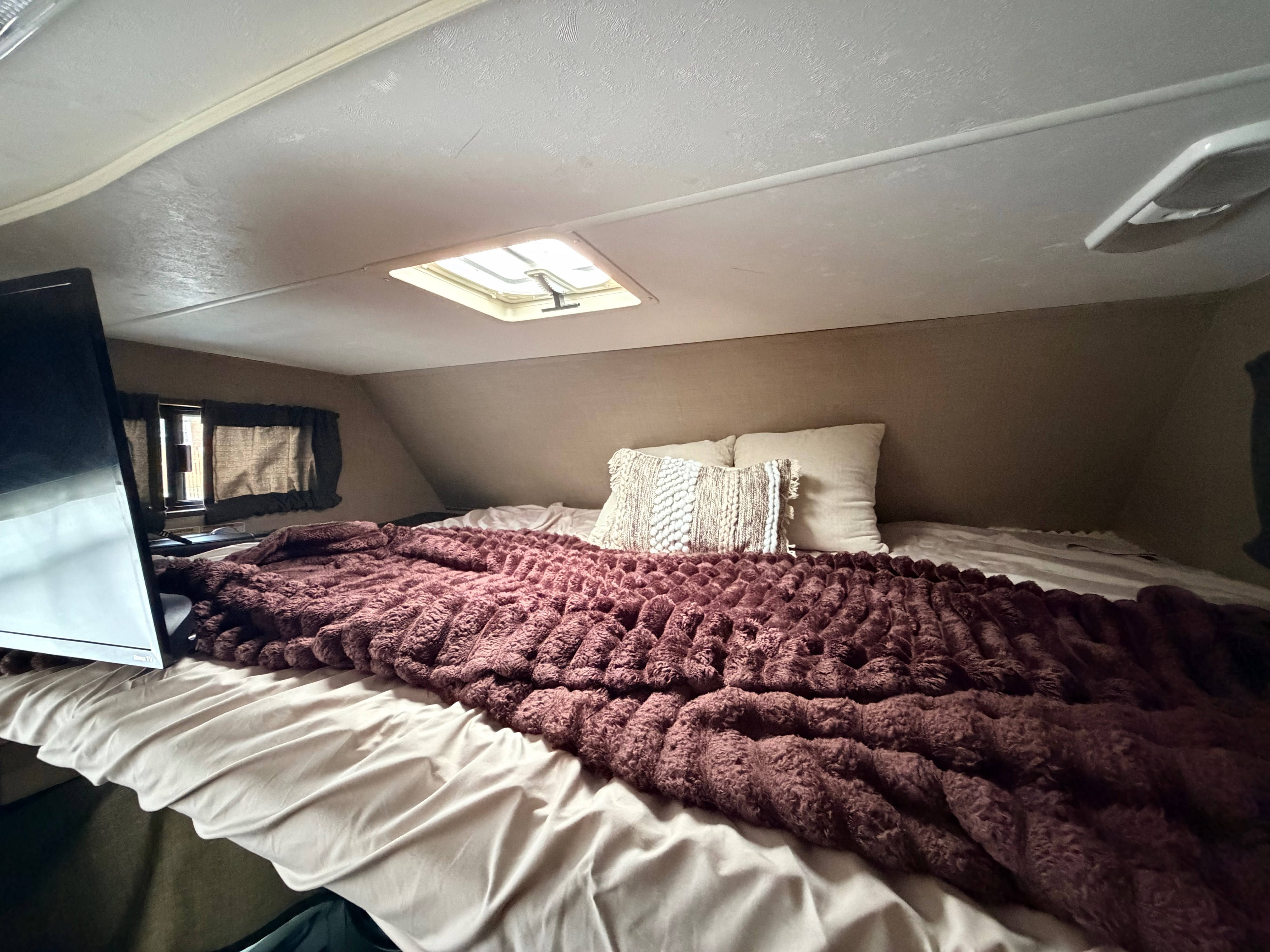 Cozy rv rental interior: a compact bedroom features a soft bed with decorative pillows, TV, and overhead vent.. Thor Majestic 2019
