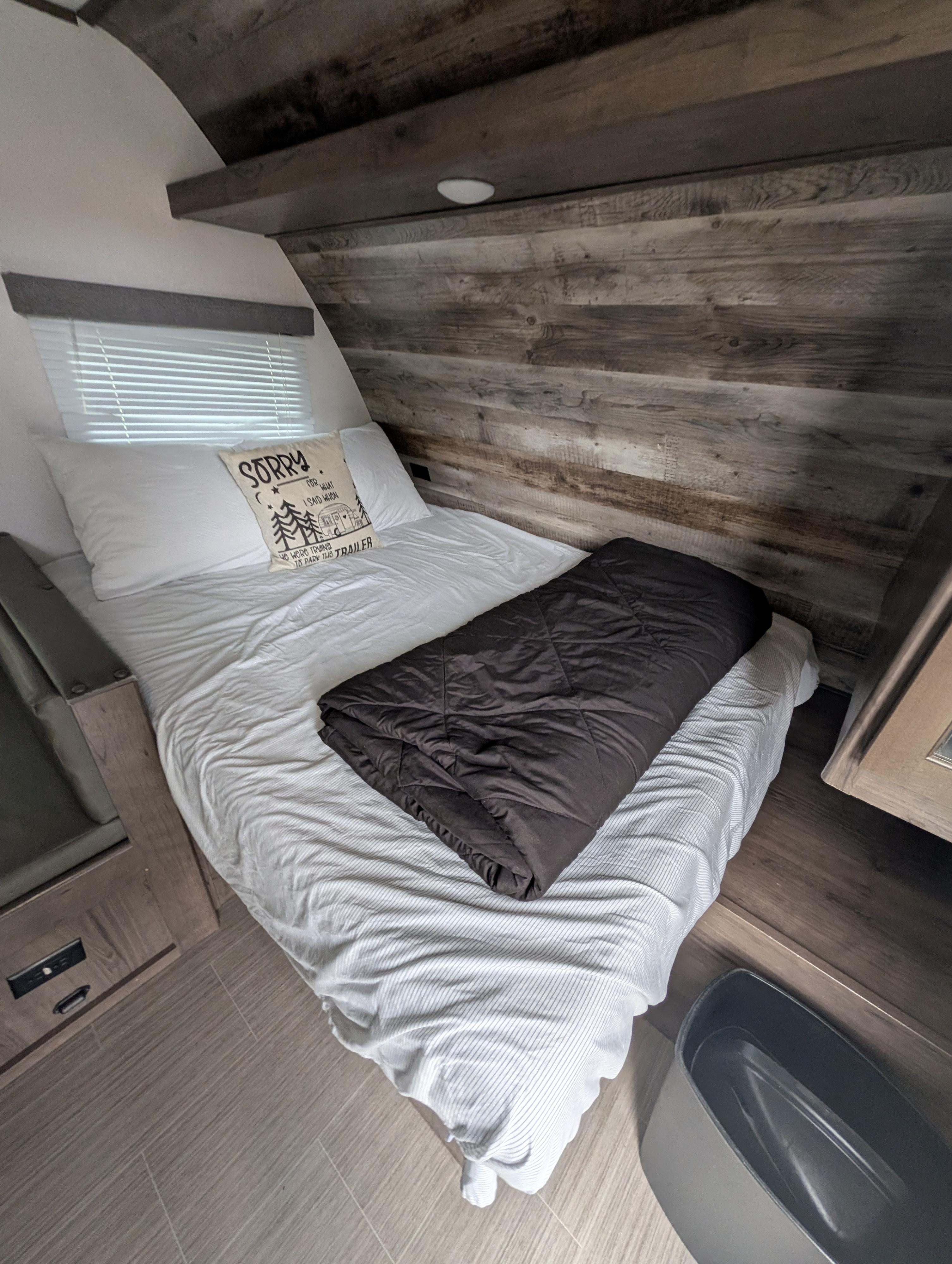 This RV rental bedroom features a bed with white sheets, a brown comforter, a fun "Sorry for what I said..." pillow, wood-paneled walls, and a window with blinds.. Other Other 2021