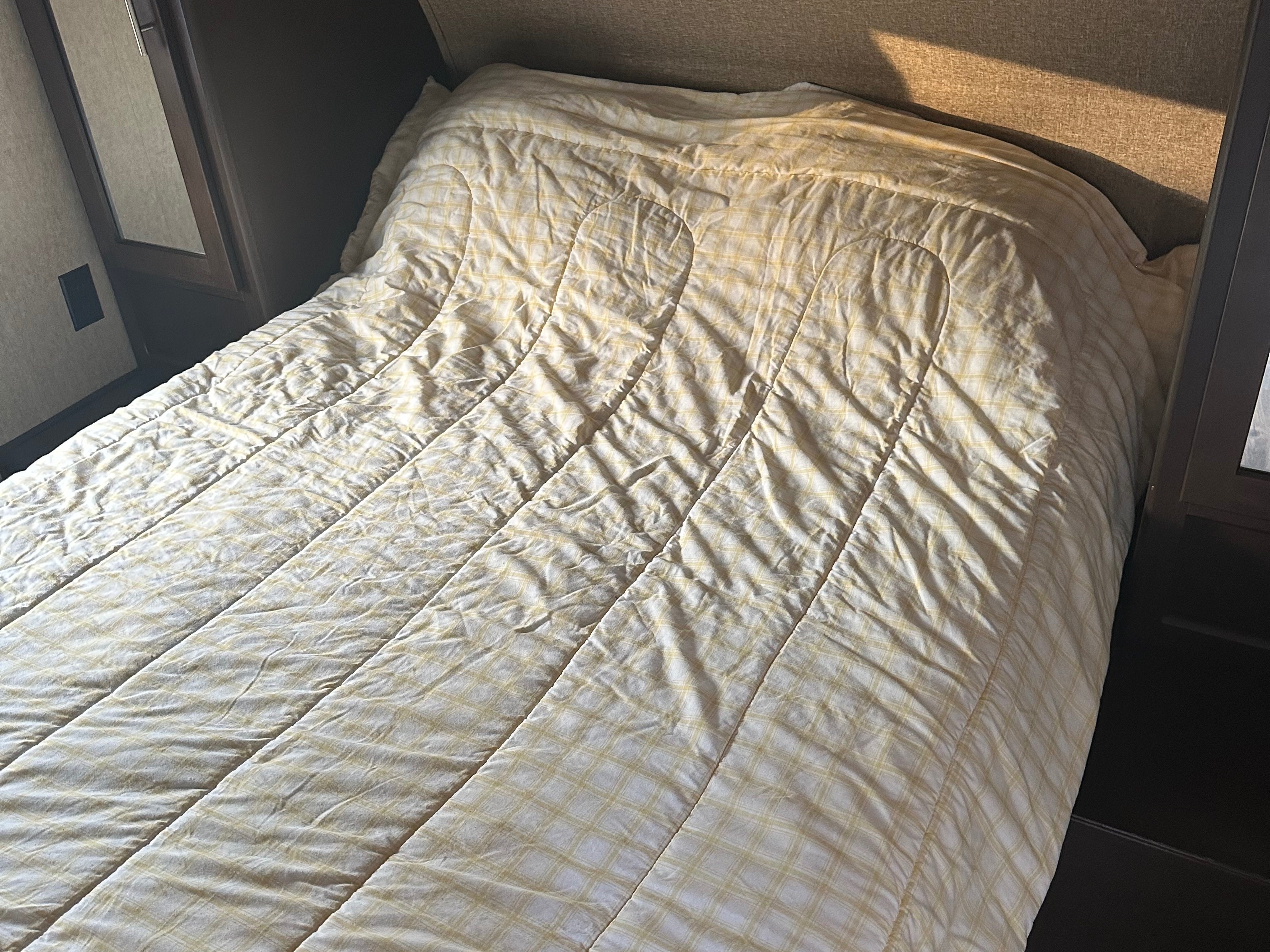 Cozy unmade bed with a yellow plaid comforter inside an RV rental, offering a comfortable sleeping area for your trip.. Forest River Grey wolf 2016