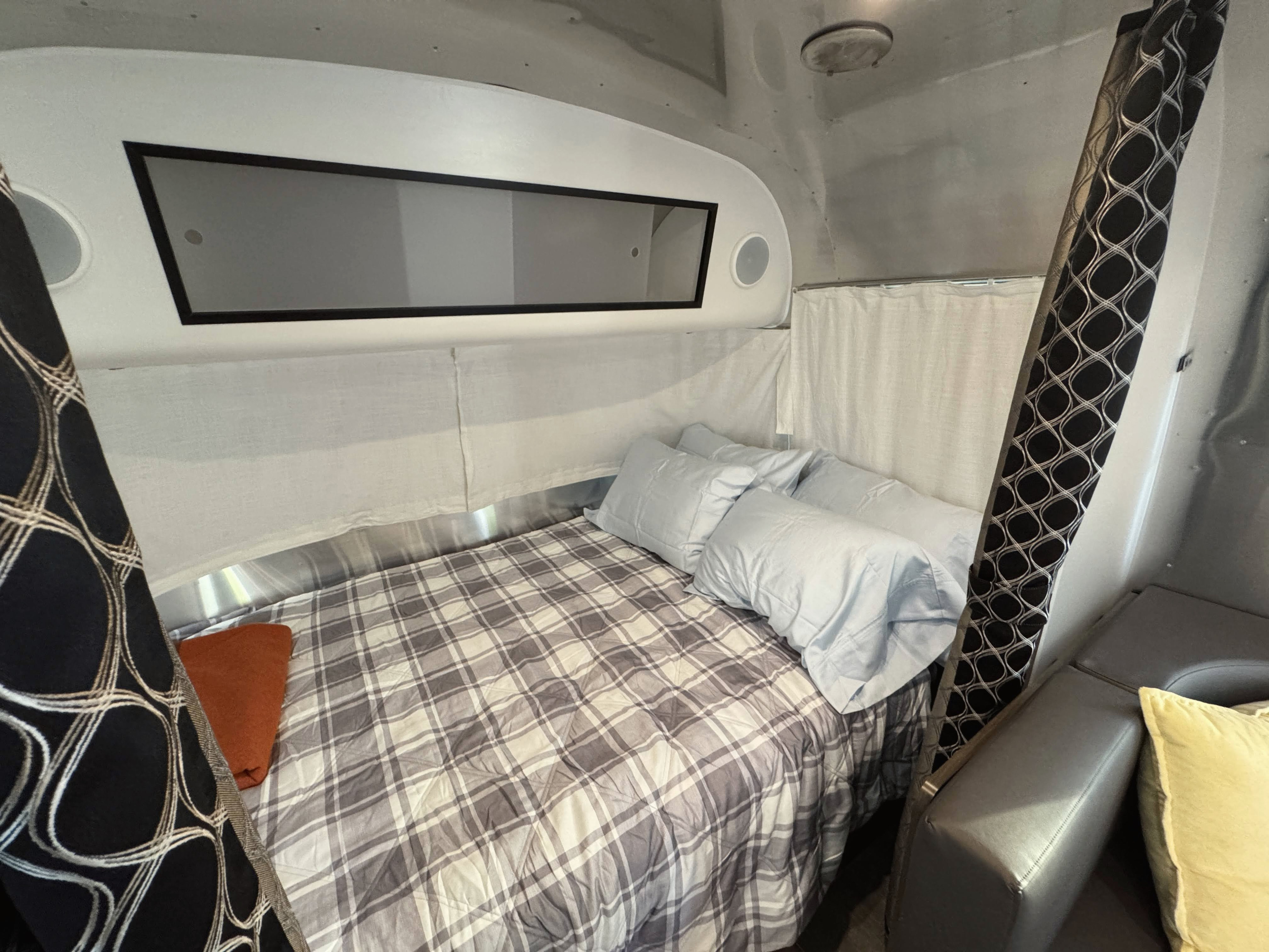 Airstream rv rental interior: a cozy bedroom with plaid bedding, soft pillows, and stylish privacy curtains for travel.. Airstream Caraval 2021