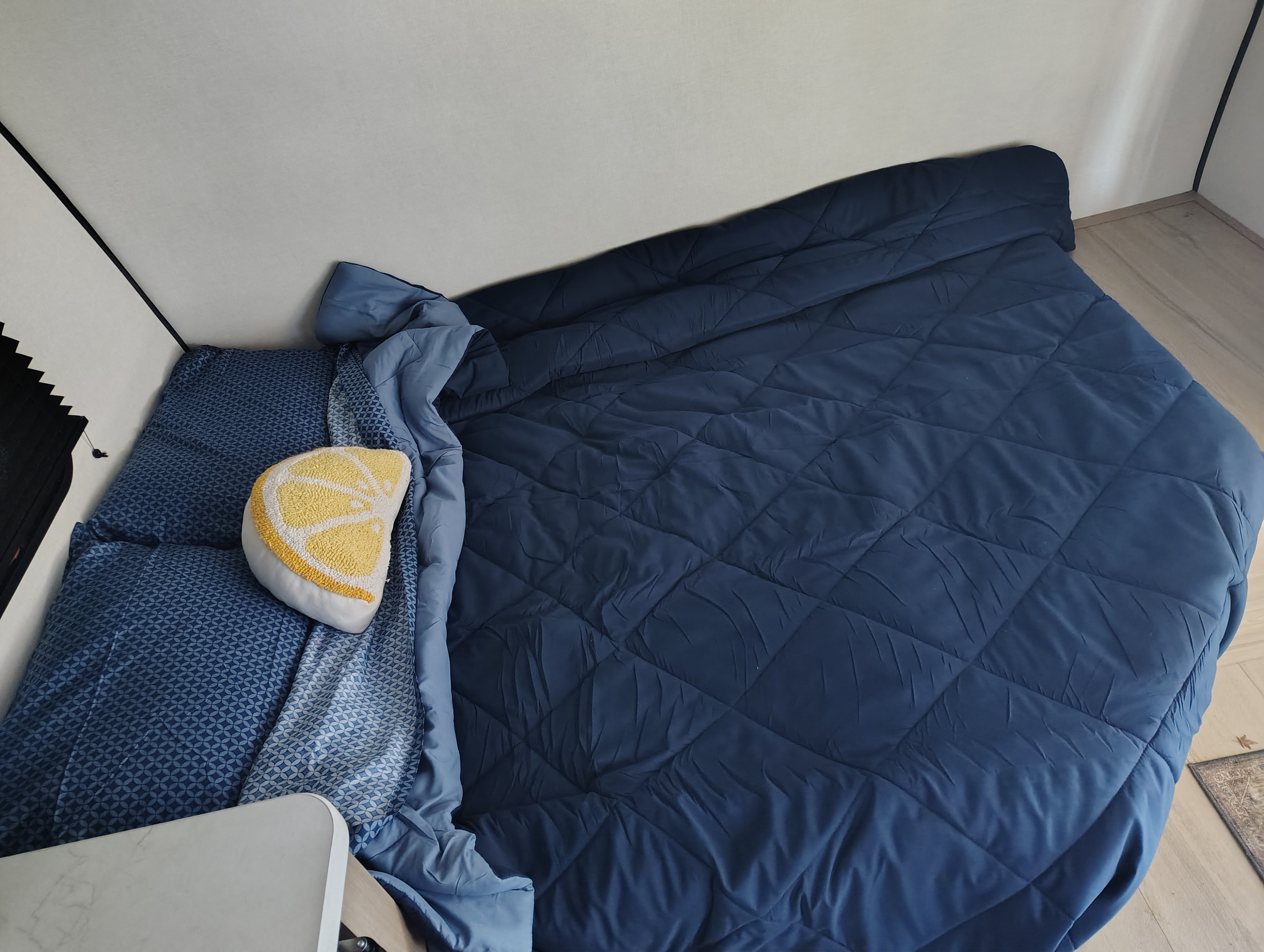 Cozy blue bed in a modern RV rental, perfect for travel. Features dark blue quilted bedding and a cheerful lemon-slice pillow.. Keystone RV Coleman 2025