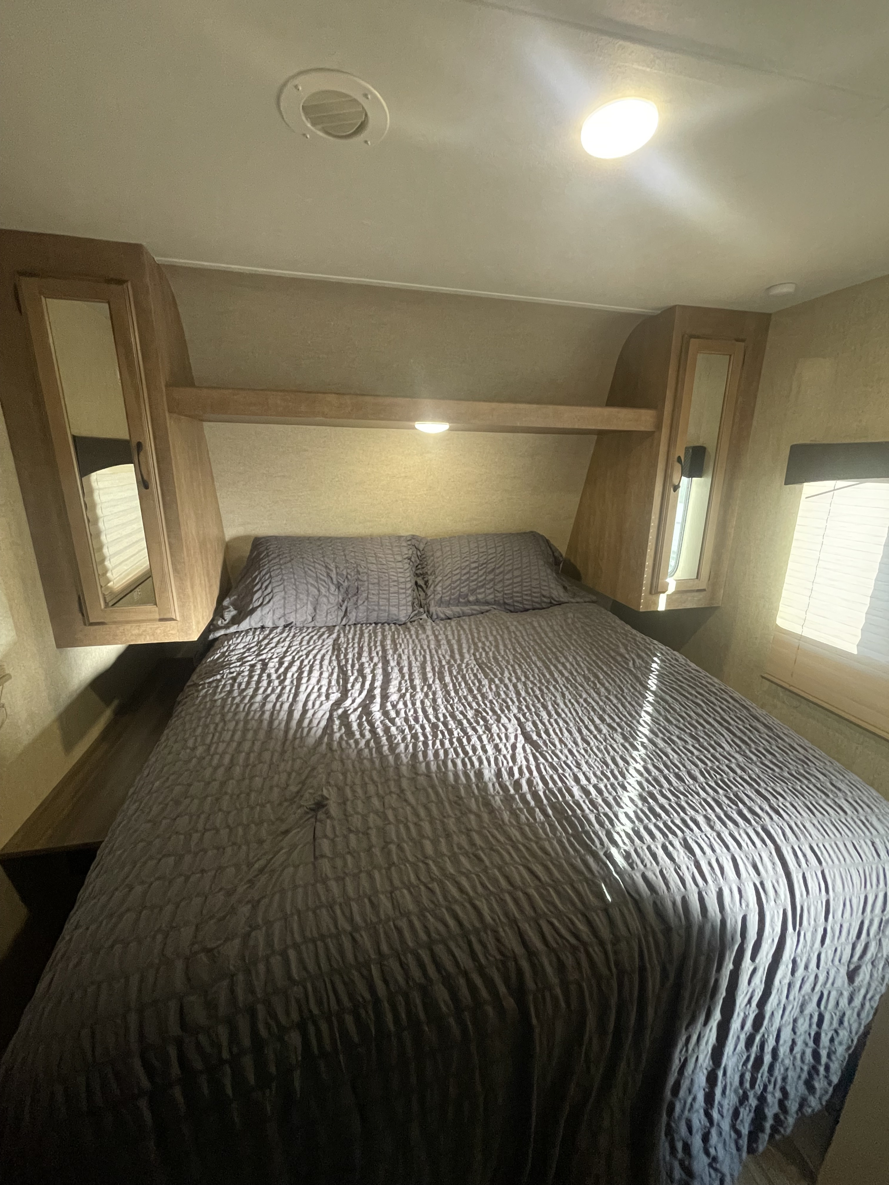 A compact RV rental bedroom with a grey bed, pillows, overhead cabinets, and a window with blinds.. Starcraft Launch Ultra Lite 2017