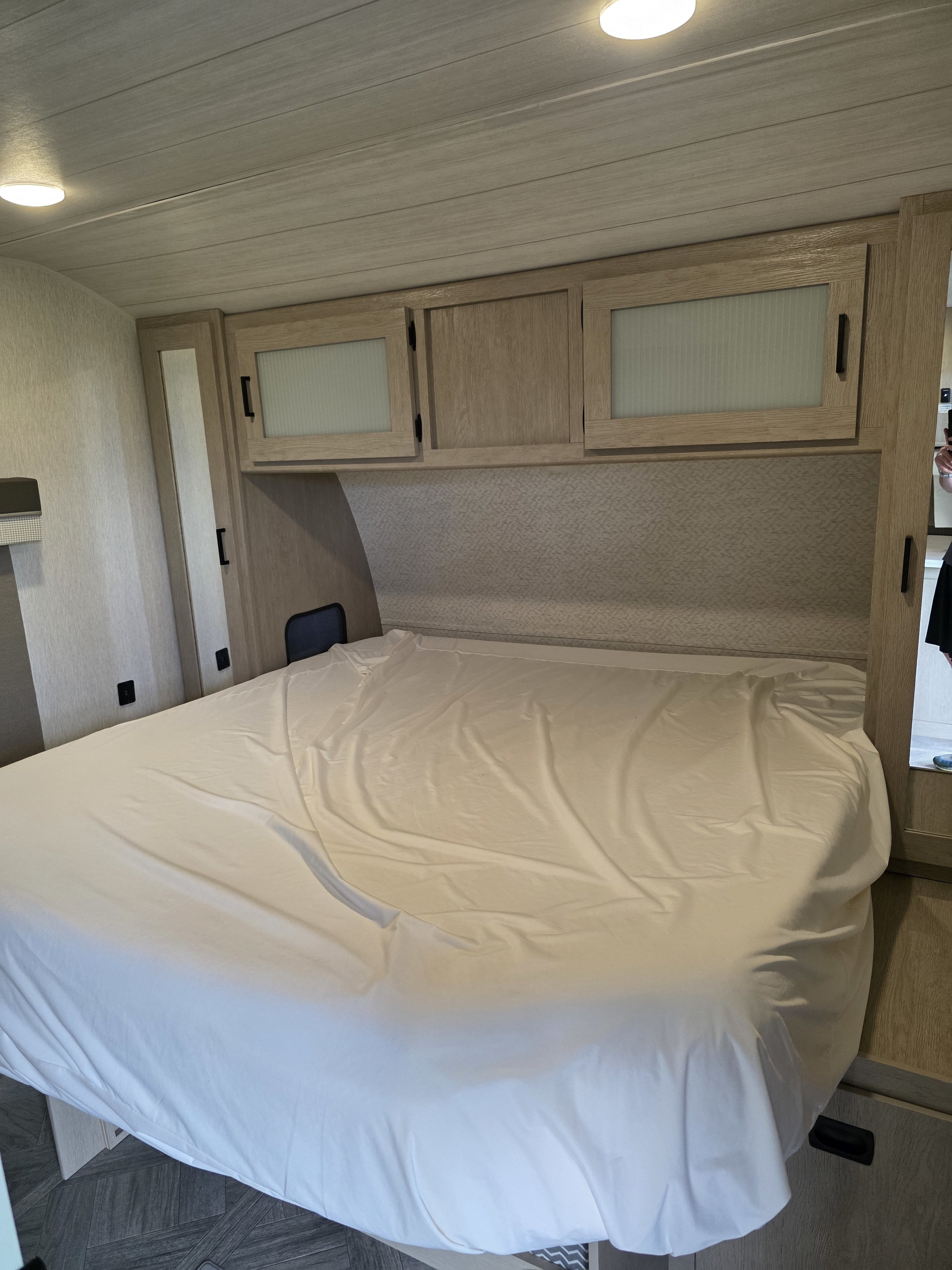 RV rental bedroom: a large bed with white sheets, light wood overhead cabinets, and built-in side storage.. Forest River Wildwood 2023