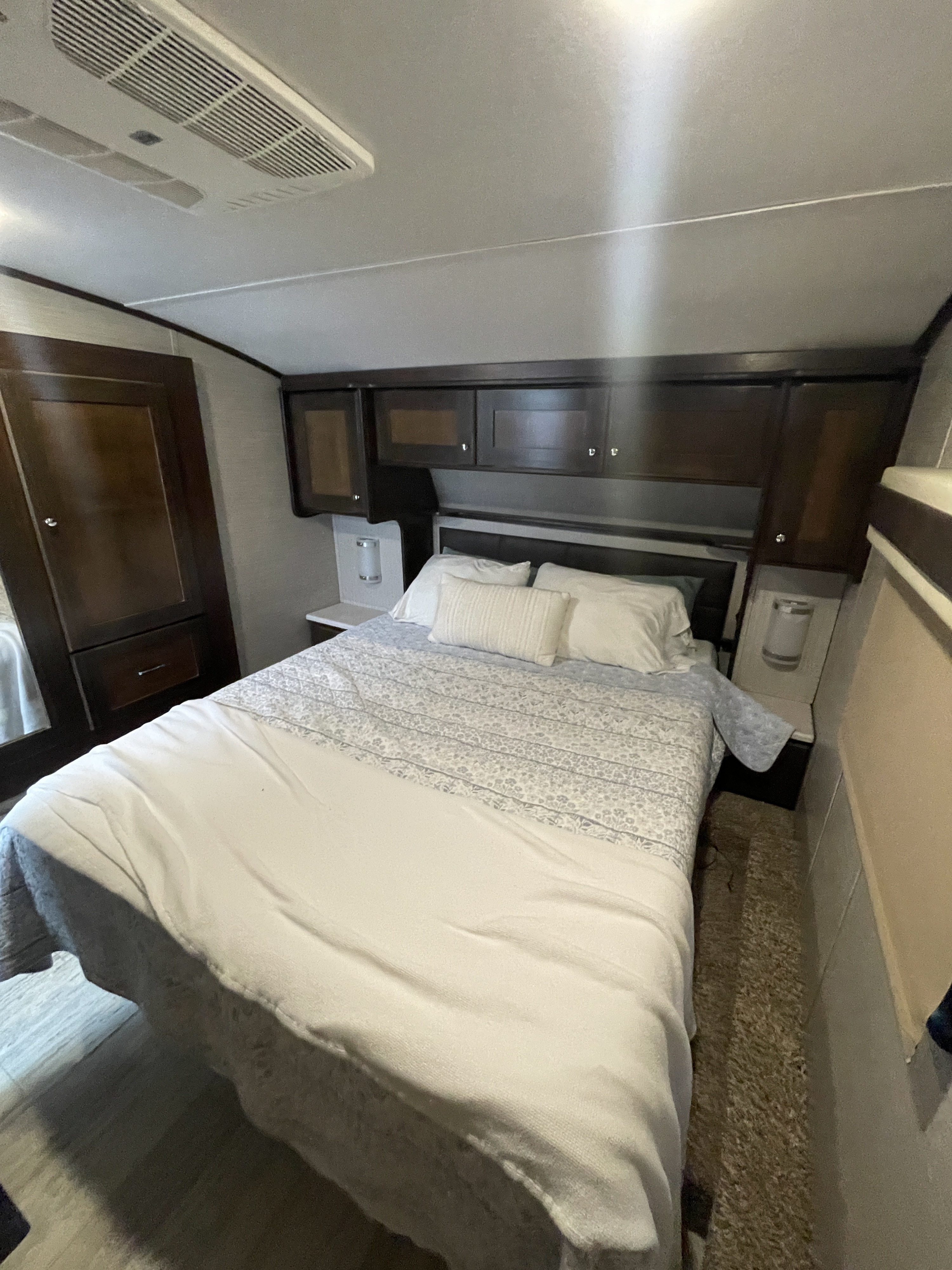 RV rental master bedroom: queen bed, overhead cabinets, side storage, and ceiling AC unit. A compact, functional travel space.. Vanleigh RV Pinecrest 2020